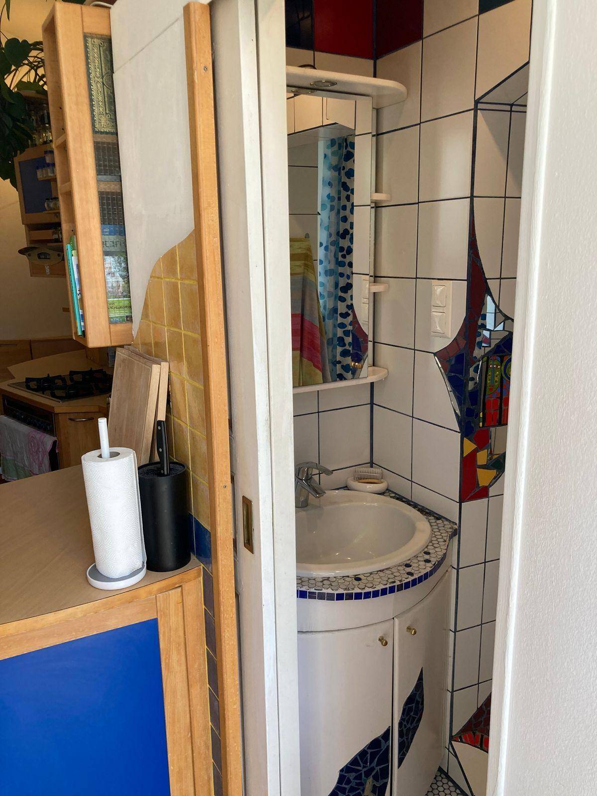 Kleines Badezimmer mit Waschbecken und farbenfrohen Fliesen, zugänglich durch eine Schiebetür.