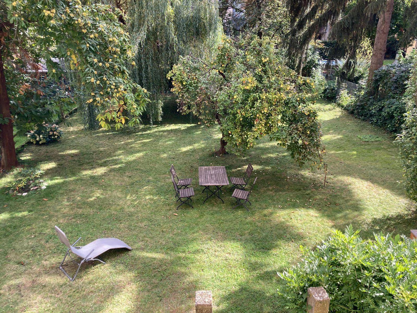 Überblick über den grünen Garten mit Rasenfläche, Bäumen und einem kleinen Essbereich im Freien.