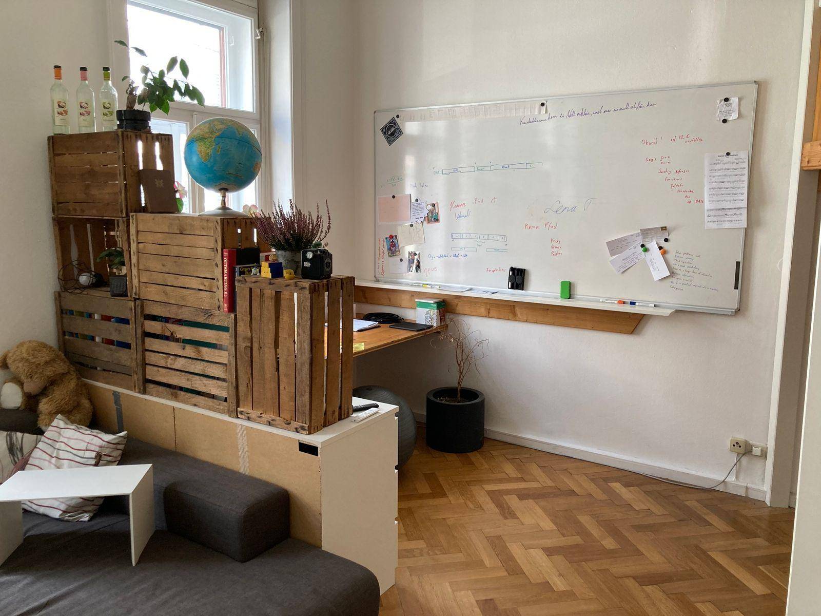 Helles Wohnzimmer mit Parkettboden, einem Sofa und einem Arbeitsbereich mit Whiteboard.