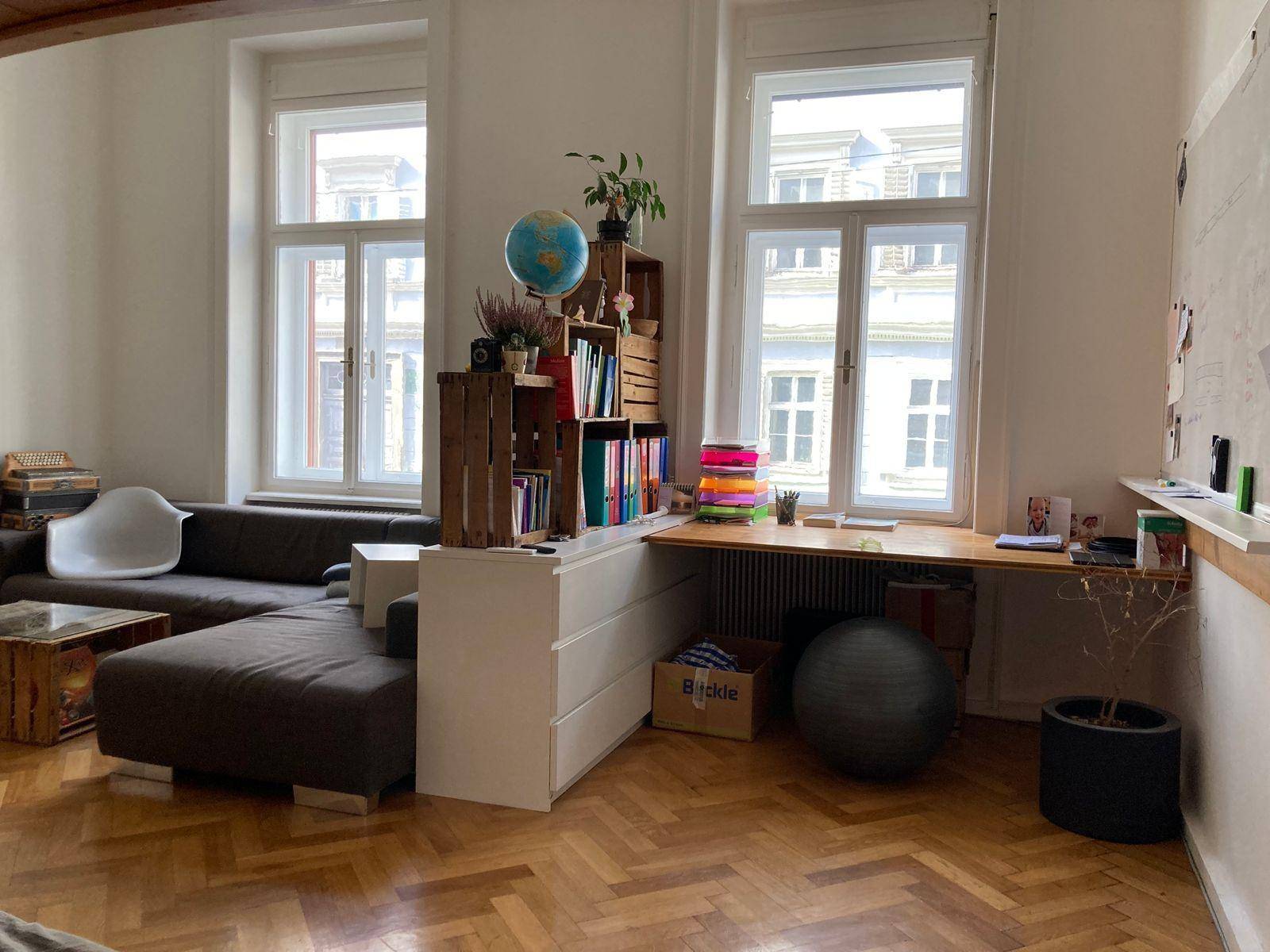 Helles Wohnzimmer mit großem Ecksofa, Arbeitsbereich und hohen Fenstern mit Stadtblick.