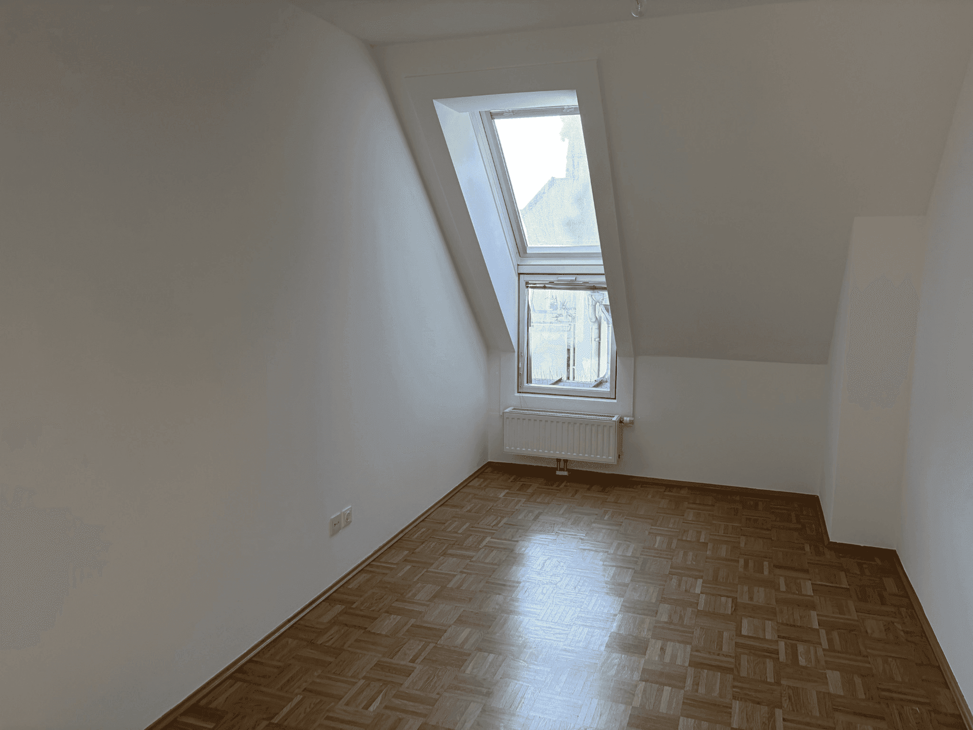 Gemütliches Zimmer mit Parkettboden, Dachschräge und Fenster für Tageslicht.
