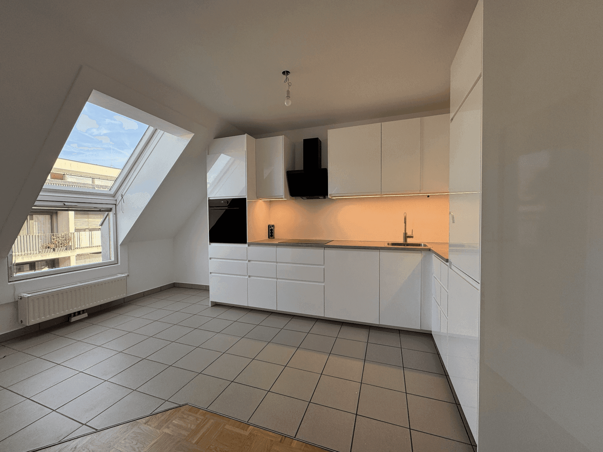 Moderne weiße Küche mit Einbaugeräten, Fliesenboden und großem Dachfenster.