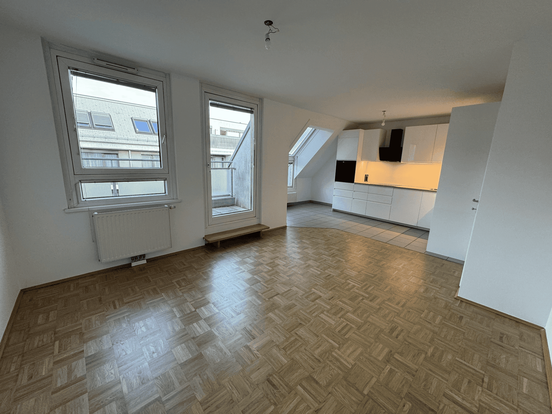 Offener Wohnbereich mit Parkettboden, Zugang zum Balkon und Blick auf die moderne Küche.