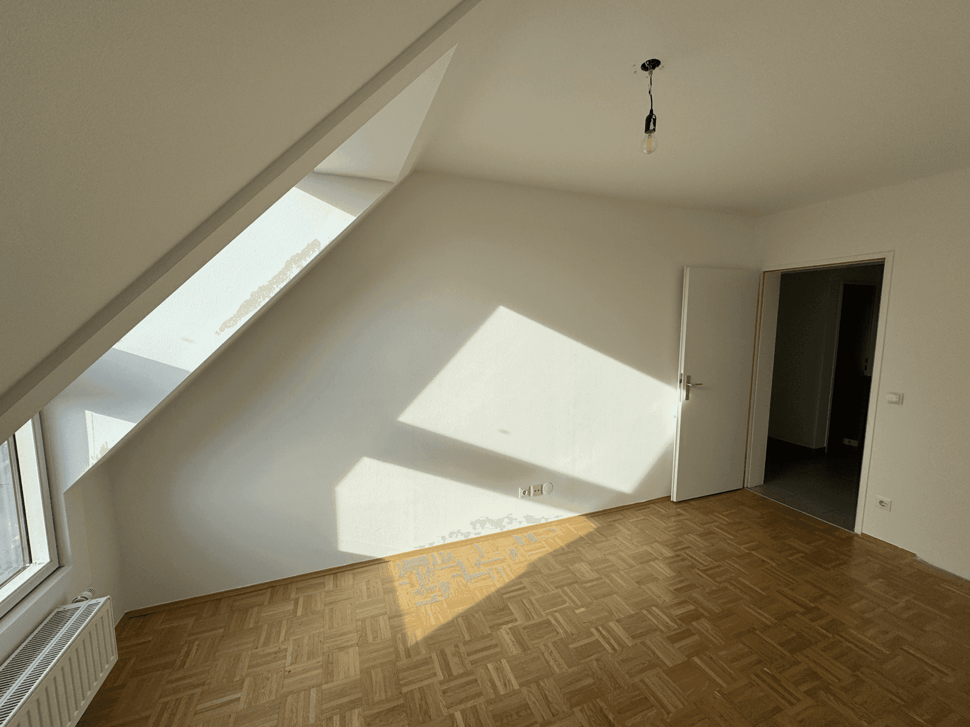 Helles Schlafzimmer mit Parkettboden, Dachschräge und viel natürlichem Lichteinfall.