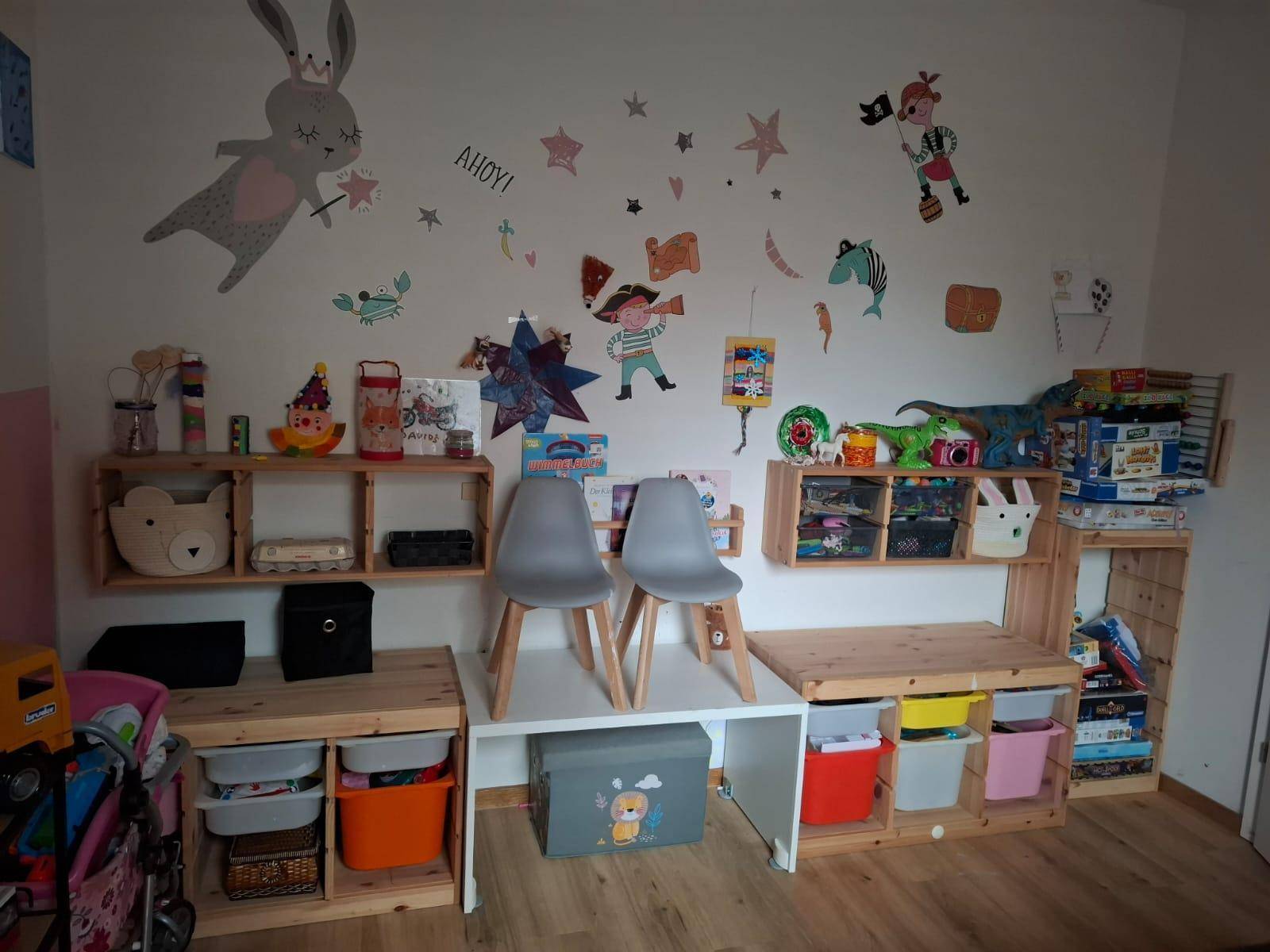 Farbenfrohes Kinderzimmer mit Spielbereich, Holzregalen und kreativen Wanddekorationen.