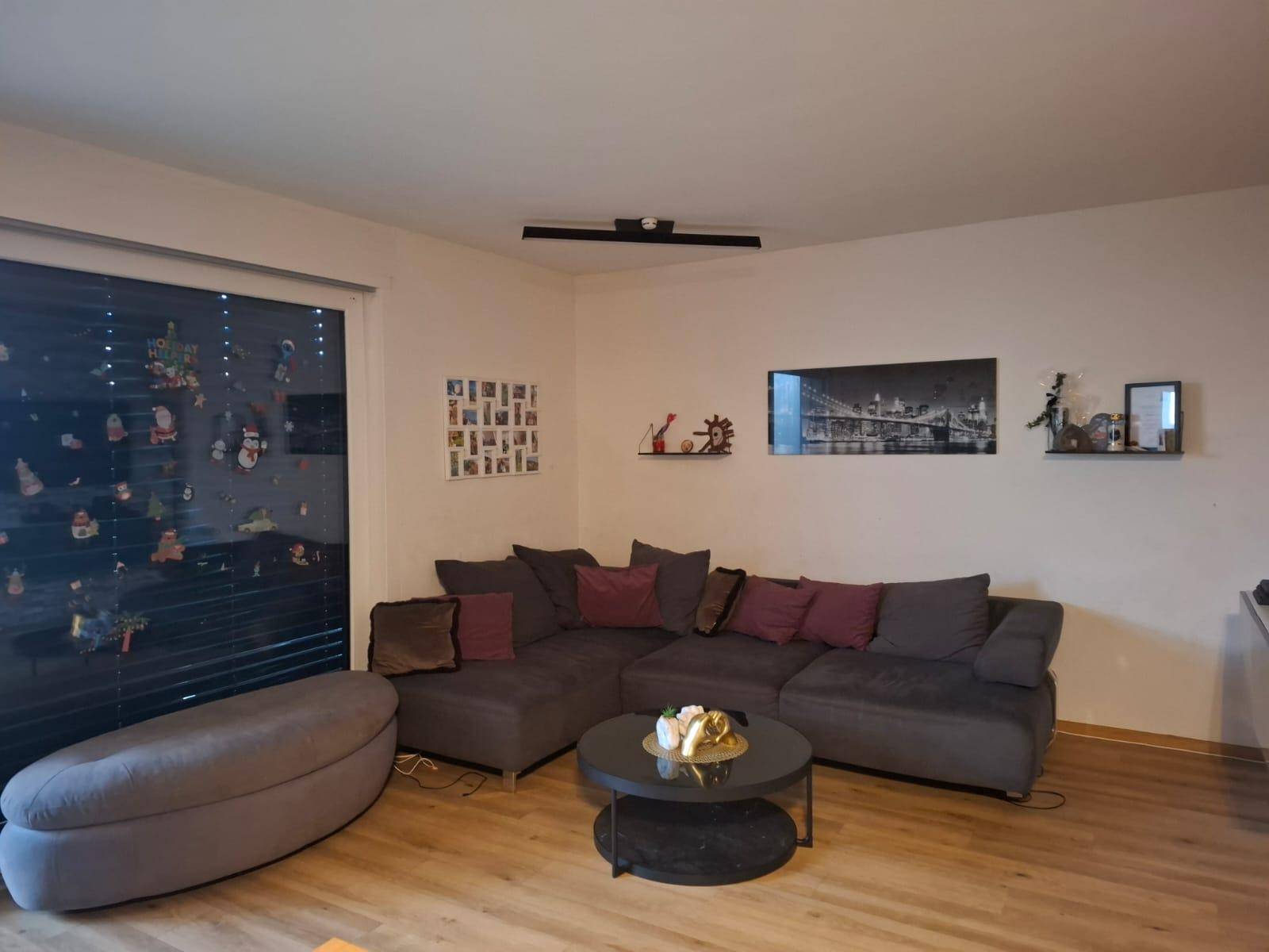 Geräumiges Wohnzimmer mit großem Ecksofa, Couchtisch und viel Tageslicht durch das Fenster.