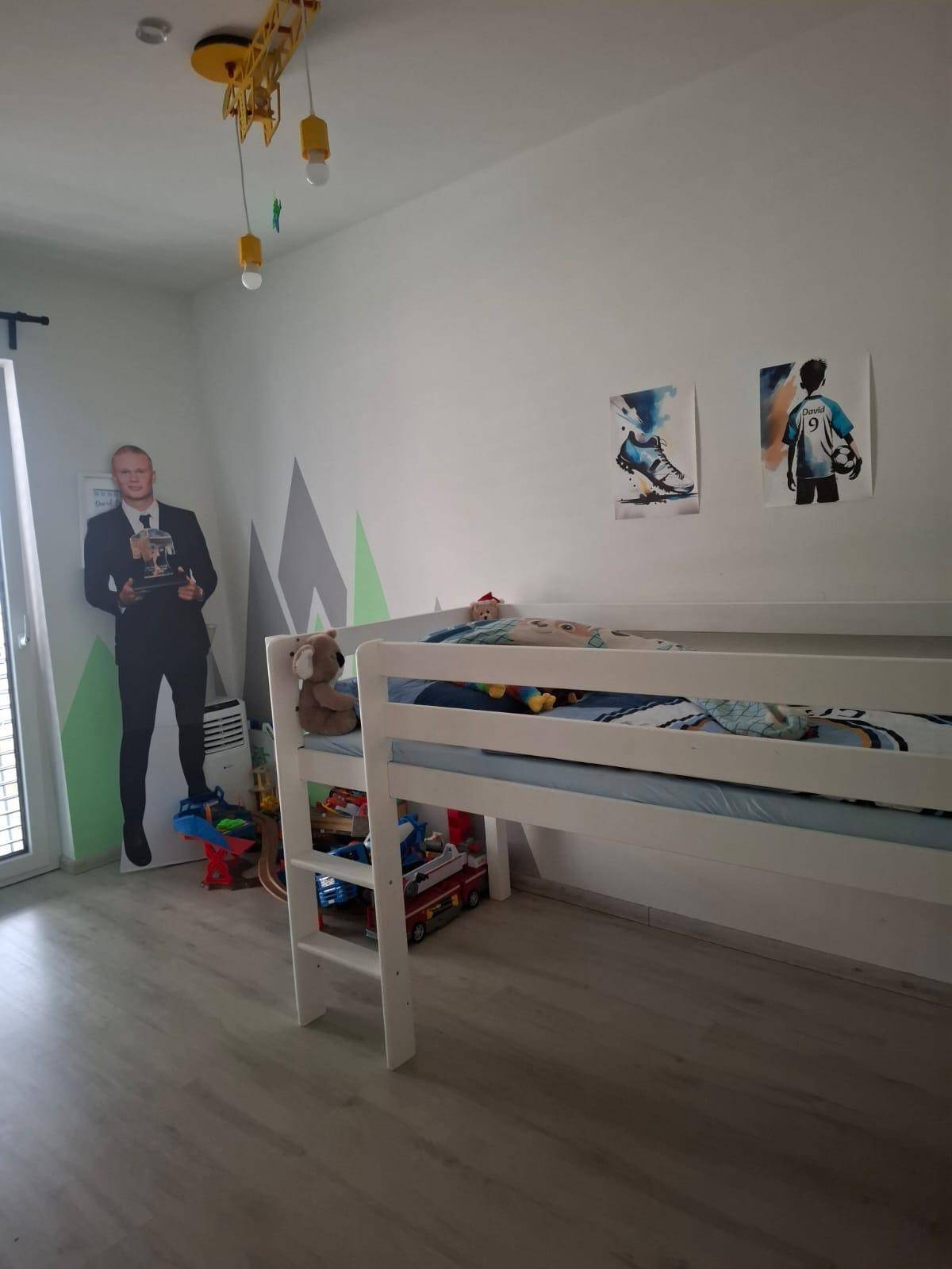Kinderzimmer mit Hochbett, Laminatboden und spielerischen Wandmalereien in Grün- und Grautönen.