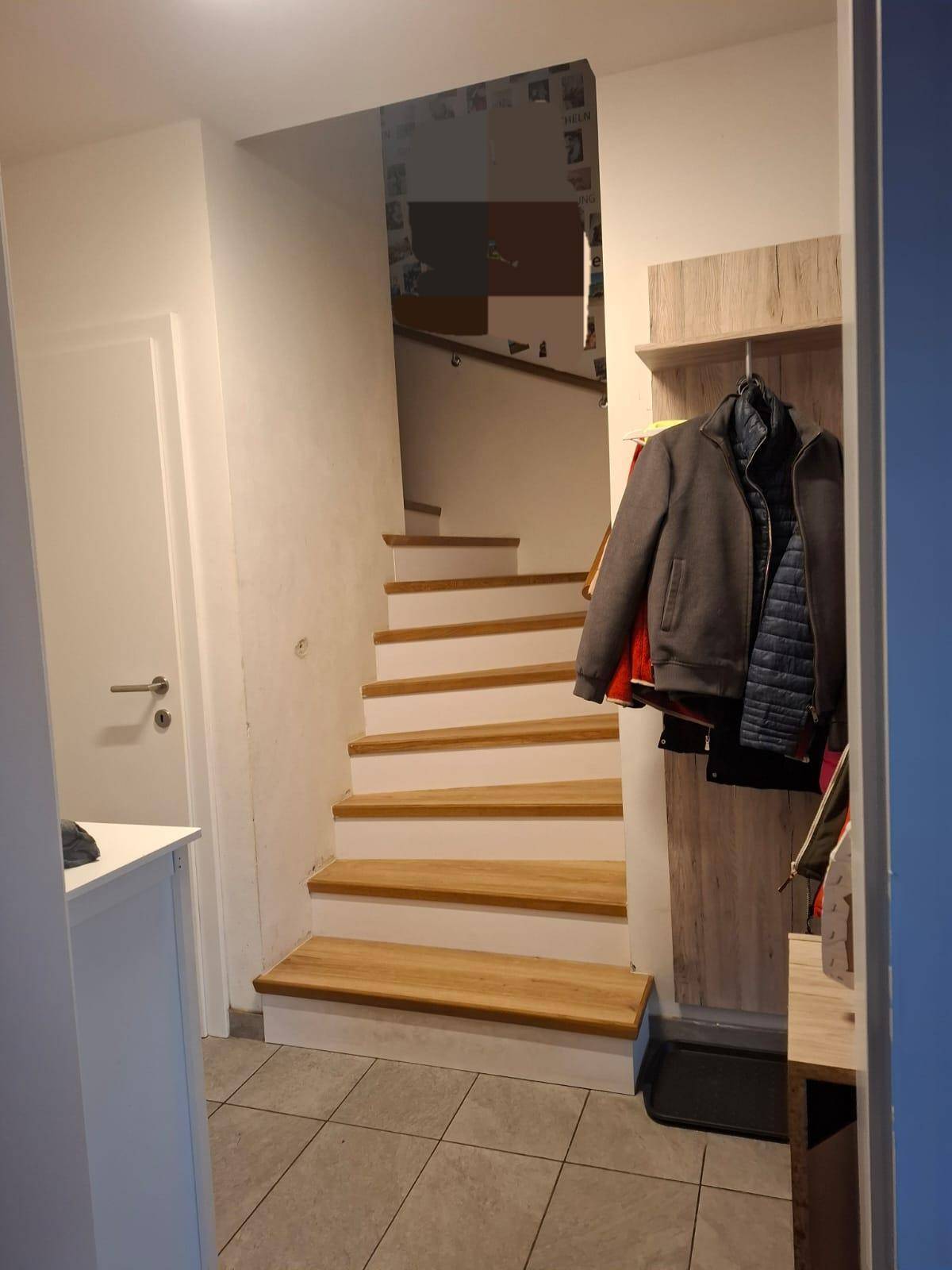 Heller Treppenaufgang mit Holzstufen und Fliesenboden im Eingangsbereich des Hauses.
