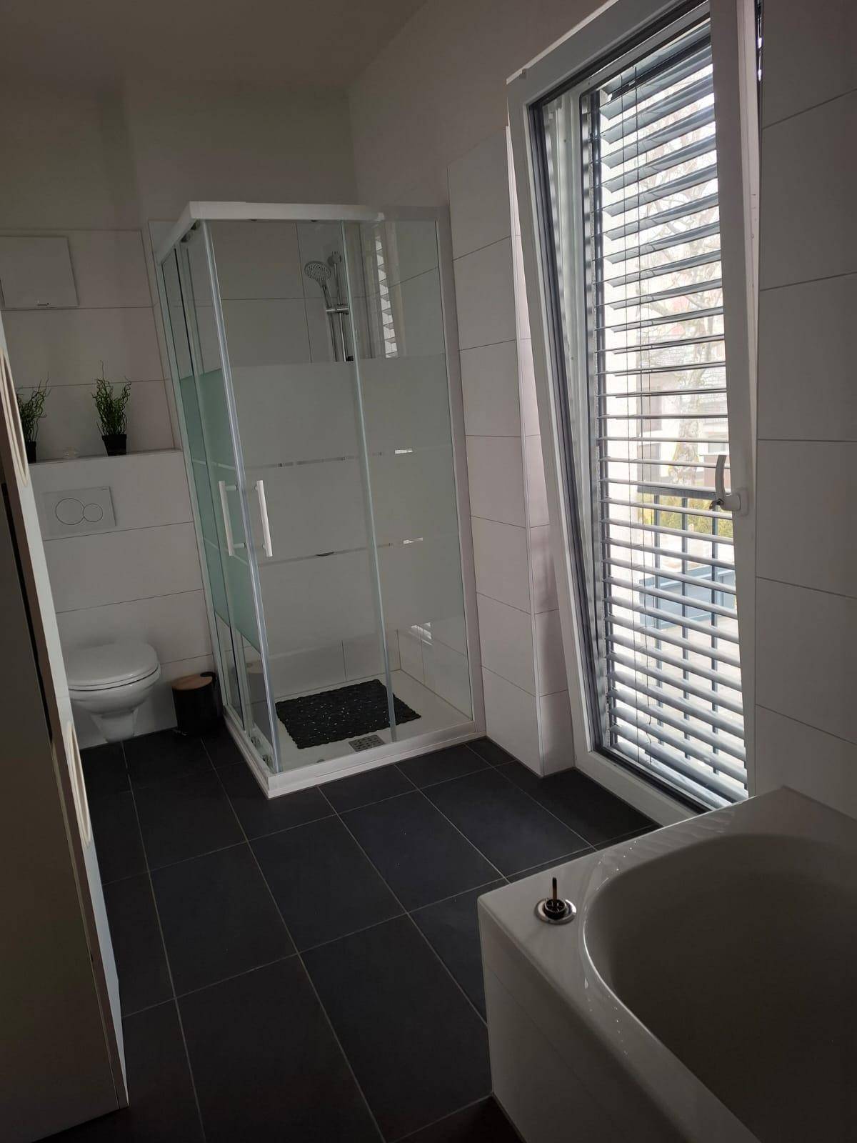 Modernes Badezimmer mit Duschkabine, Badewanne, WC und großem Fenster für Tageslicht.