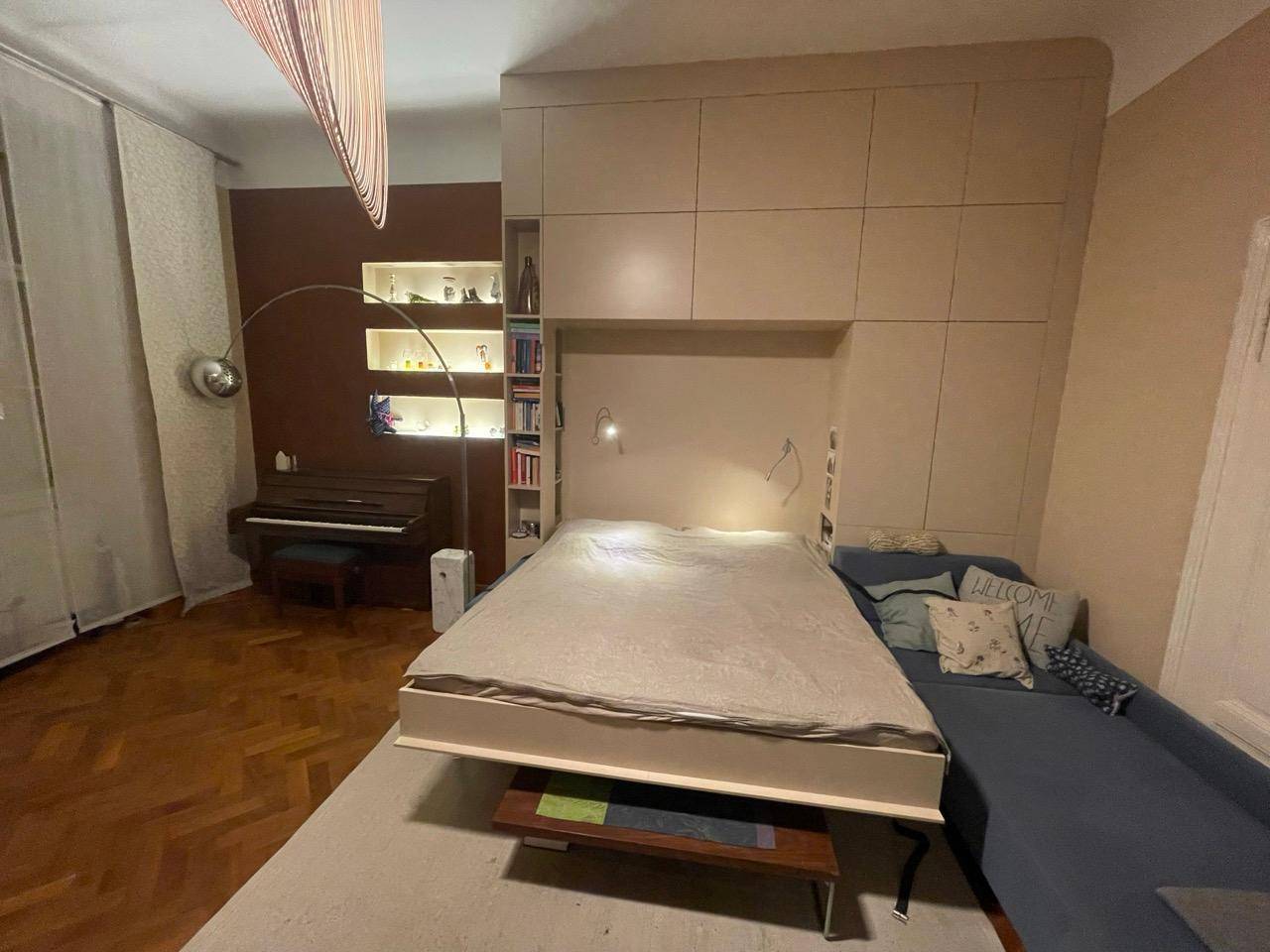 Schlafzimmer mit ausgeklapptem Schrankbett und Sofa, kombiniert Wohn- und Schlafbereich.