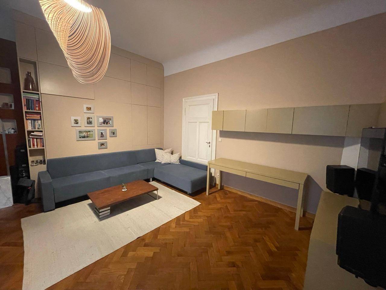 Geräumiges Wohnzimmer mit großem Sofa, Schreibtisch und Parkettboden, vielseitig nutzbar.
