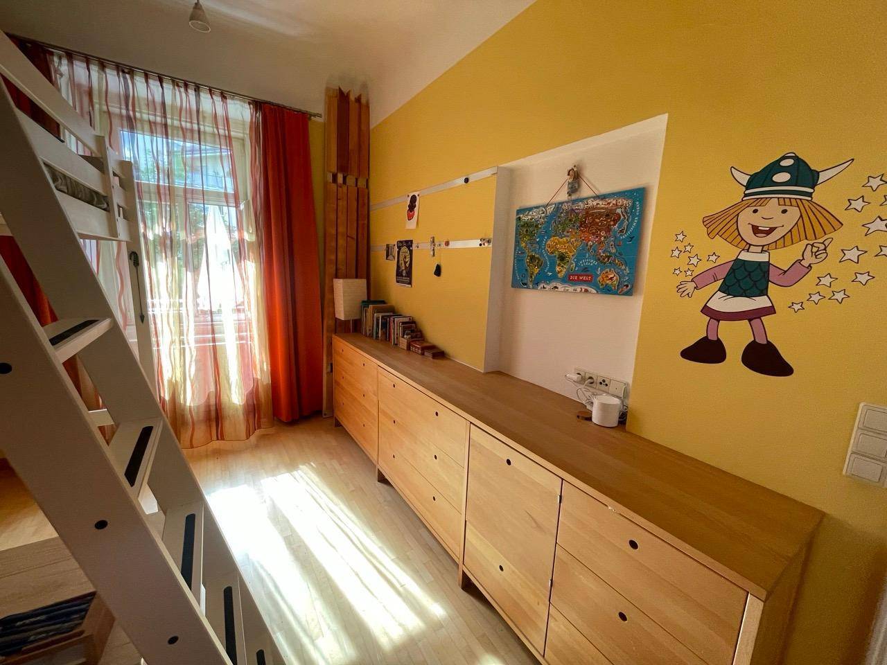 Kinderzimmer mit langen Kommoden, bunten Wanddekorationen und Parkettboden.