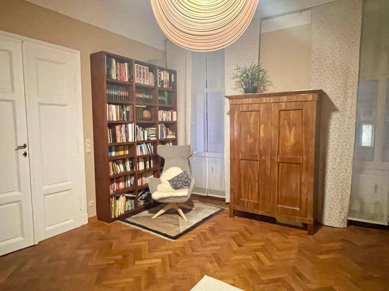 Gemütliches Wohnzimmer mit Bücherregal, Sessel und Parkettboden, ideal zum Entspannen.