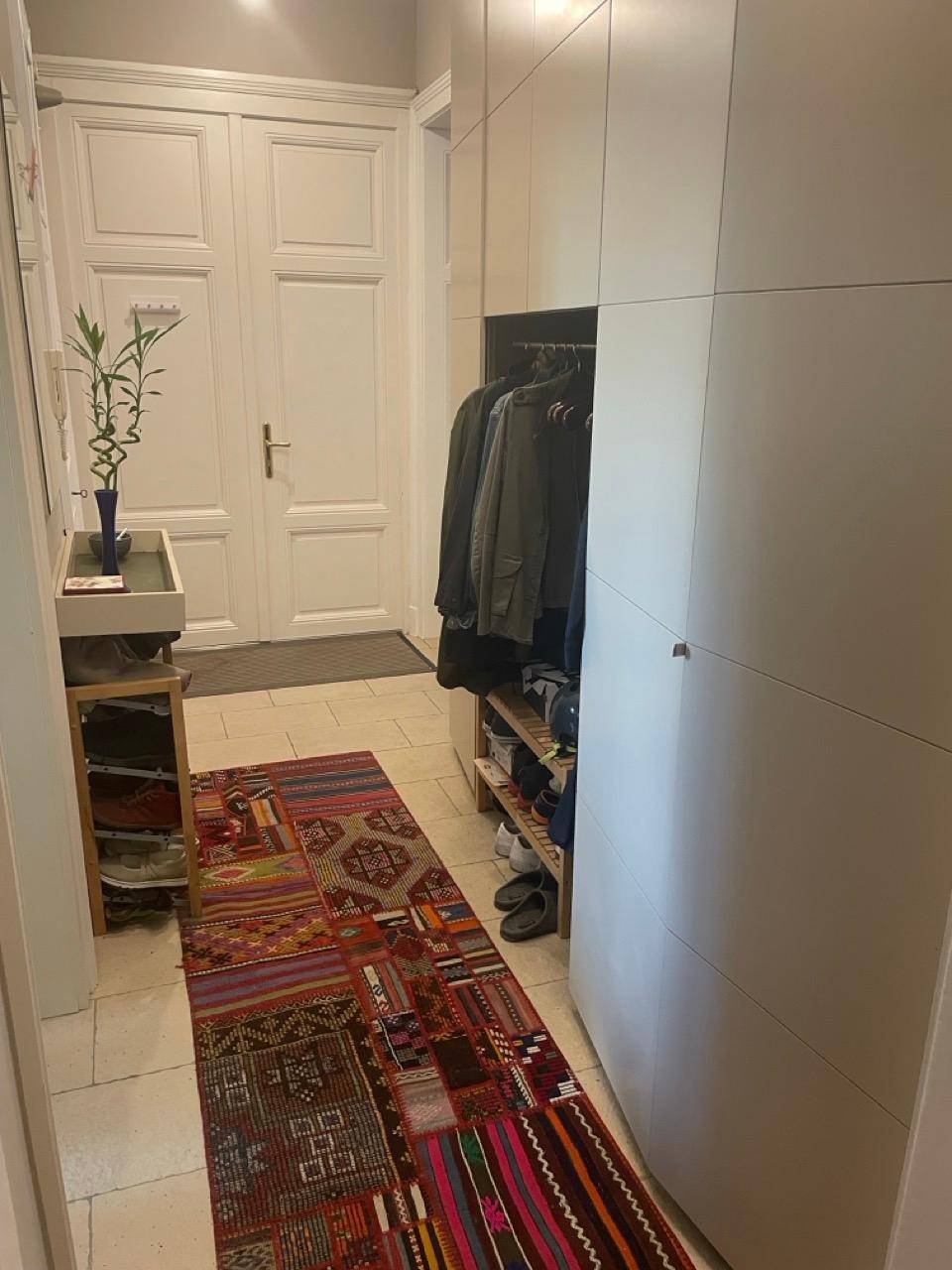 Heller Eingangsbereich mit Einbauschränken, Schuhregal und farbenfrohem Teppich.
