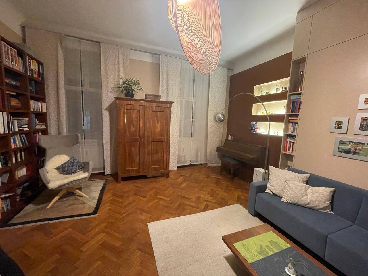 Wohnzimmer mit Sofa, Klavier, Bücherregalen und Parkettboden, hell und einladend.
