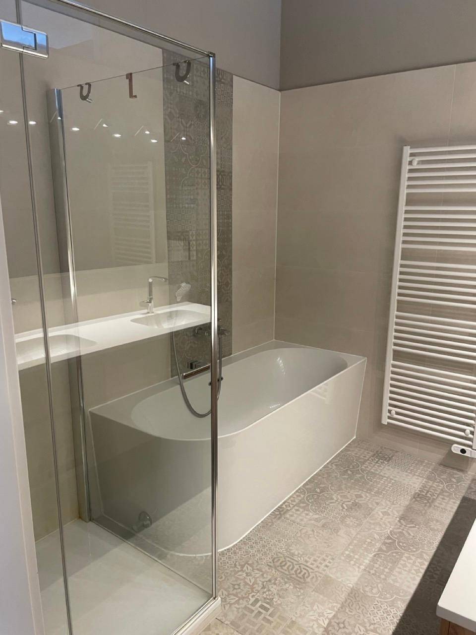Modernes Badezimmer mit Badewanne, Duschkabine und beheiztem Handtuchhalter.