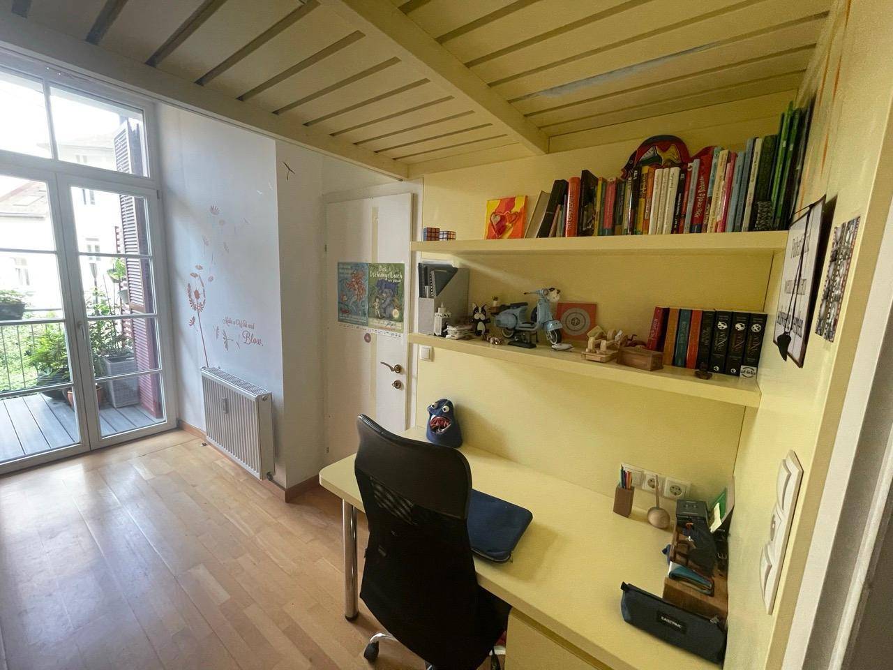 Kinderzimmer mit Schreibtisch, Regalen und Zugang zum Balkon, hell und funktional.