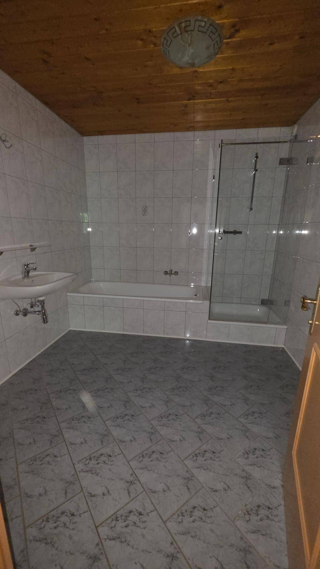 Gefliestes Badezimmer mit Badewanne, Duschkabine, Waschbecken und Holzdecke.