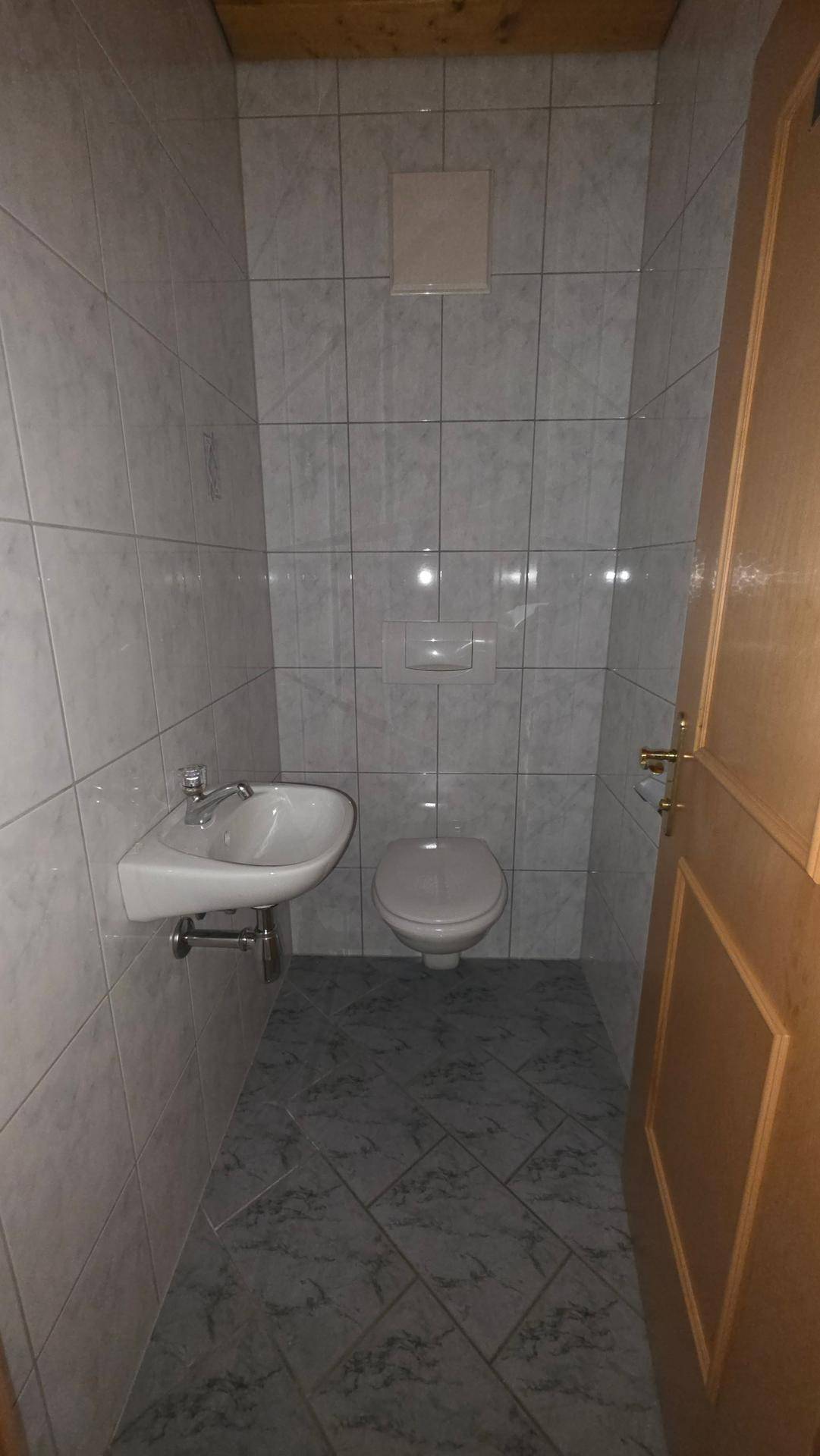 Kleines Gäste-WC mit Wand-WC, Waschbecken, gefliesten Wänden und Holzdecke.