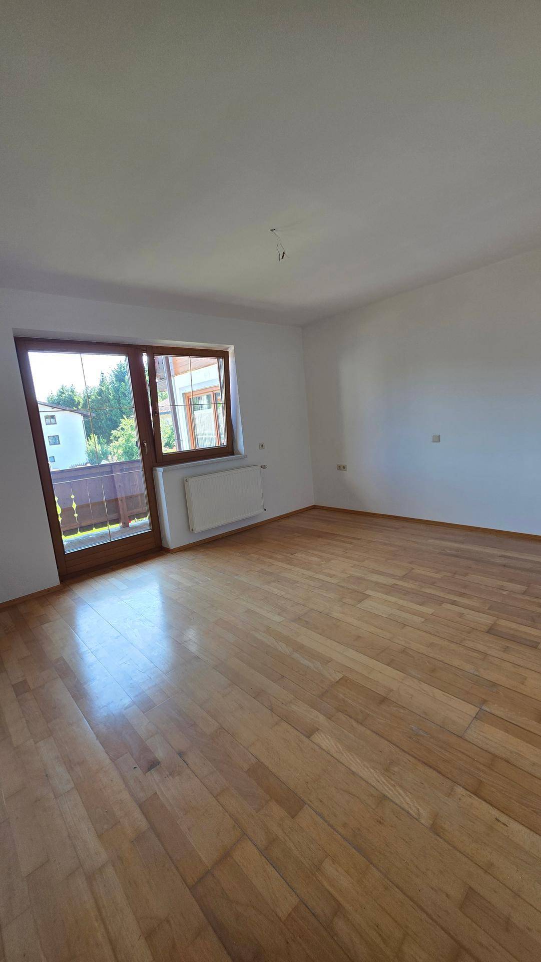 Geräumiges Zimmer mit Parkettboden, weißen Wänden und Zugang zu einem Balkon.
