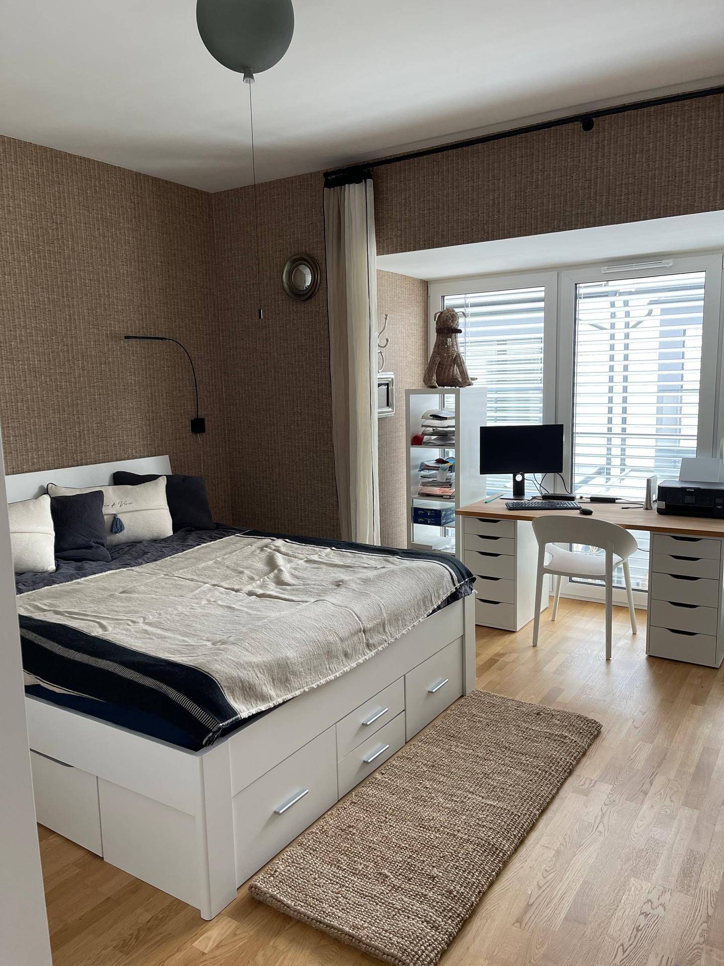 Schlafzimmer mit integriertem Arbeitsbereich, Holzboden und großen Fenstern.