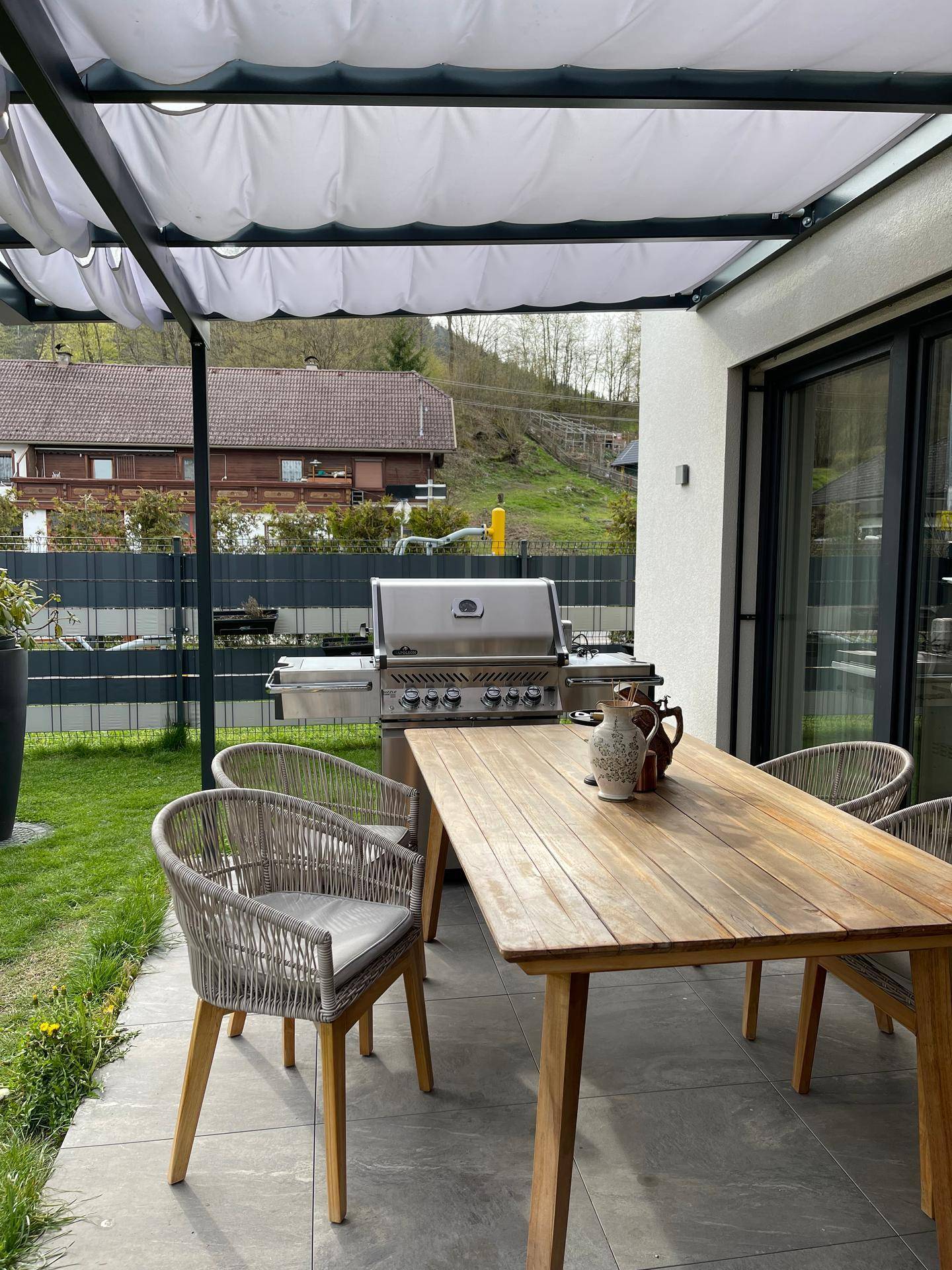 Überdachter Essbereich auf der Terrasse mit großem Grill und Blick ins Grüne.