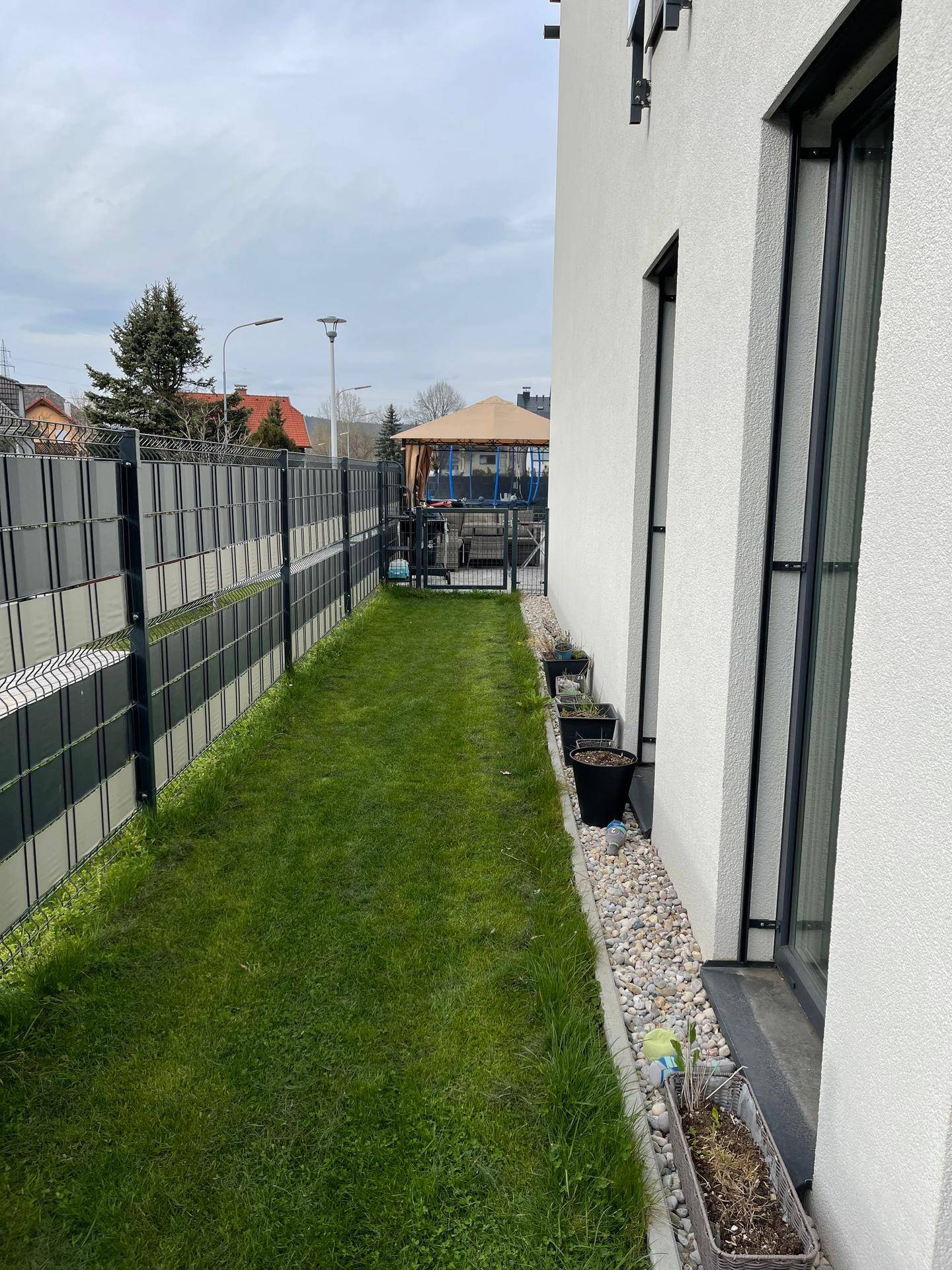 Schmaler Gartenbereich entlang des Hauses mit Rasenfläche und modernem Zaun.