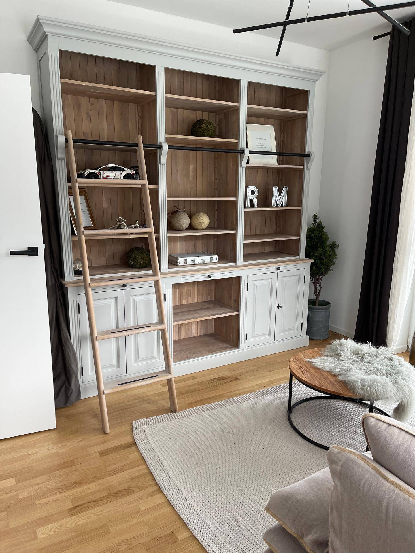 Geräumiges Wohnzimmer mit großem Bücherregal, Holzboden und hellem Teppich.