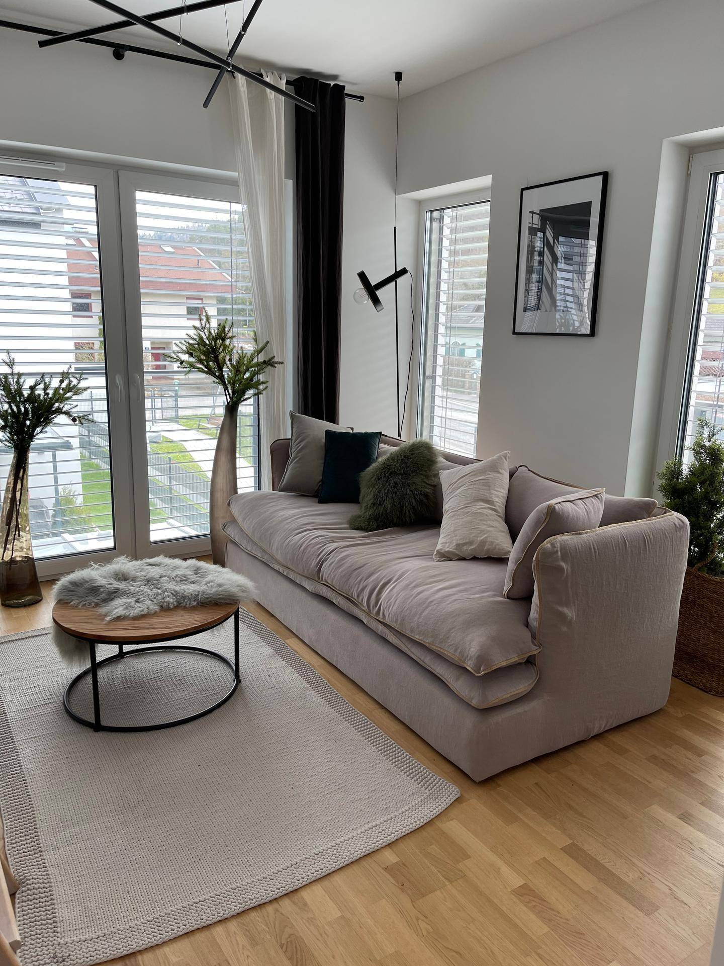 Helles Wohnzimmer mit beigem Sofa, Holzboden und großen Fenstern für viel Tageslicht.