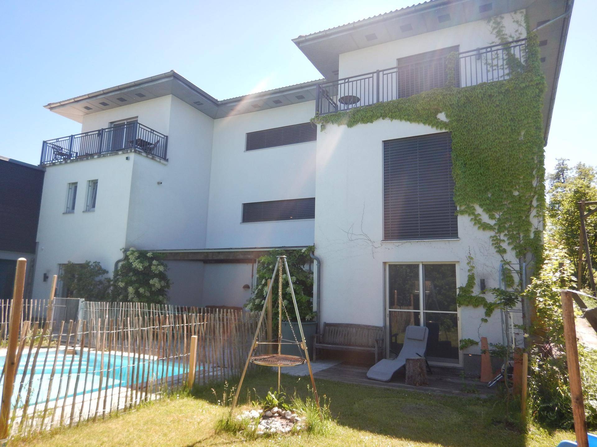 Seitliche Ansicht des modernen Hauses mit Pool, Gartenbereich und einer Schaukel im Grünen.