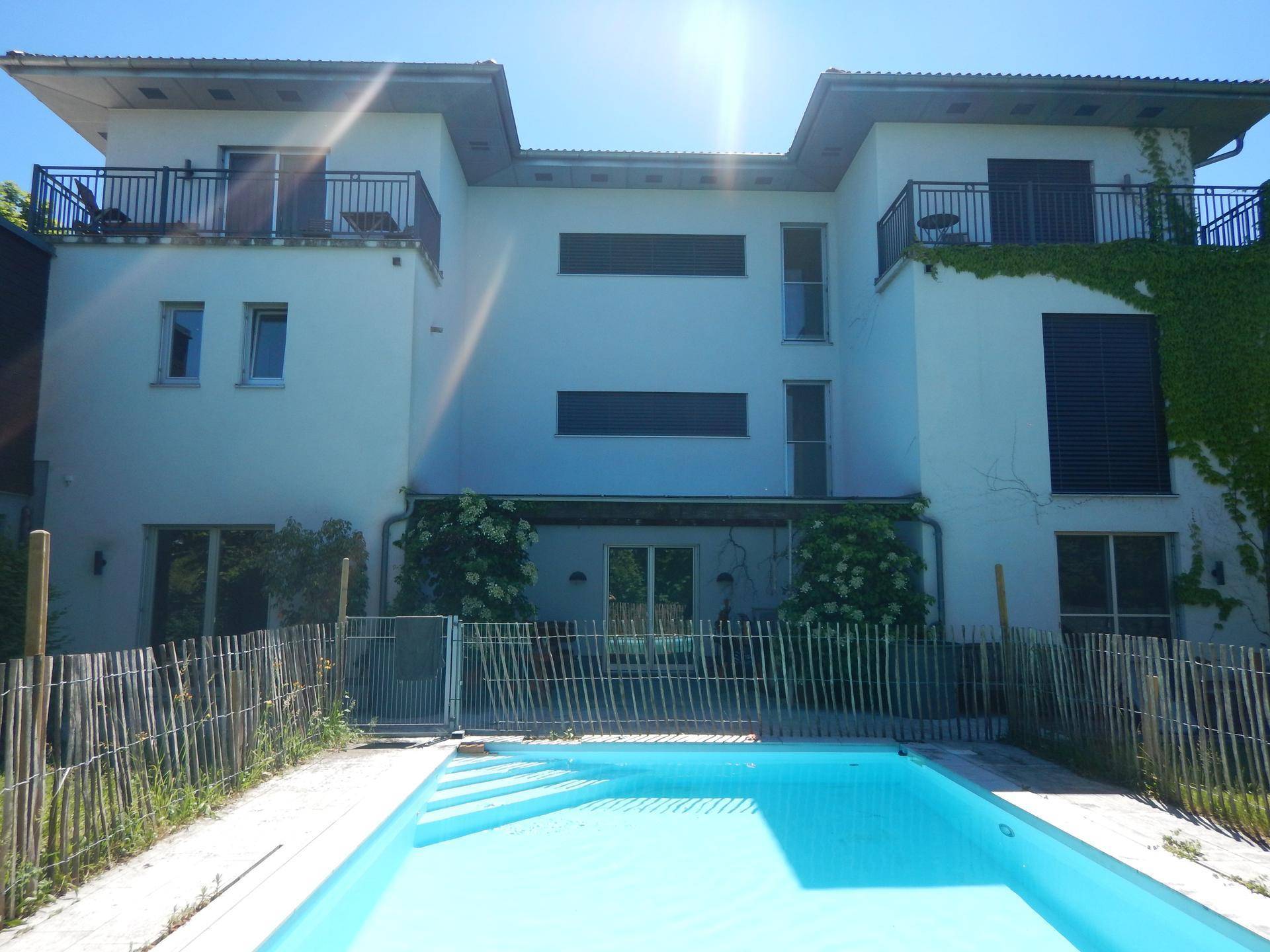 Moderne Hausfassade mit Balkonen, Terrasse und einem erfrischenden Swimmingpool im Gartenbereich.