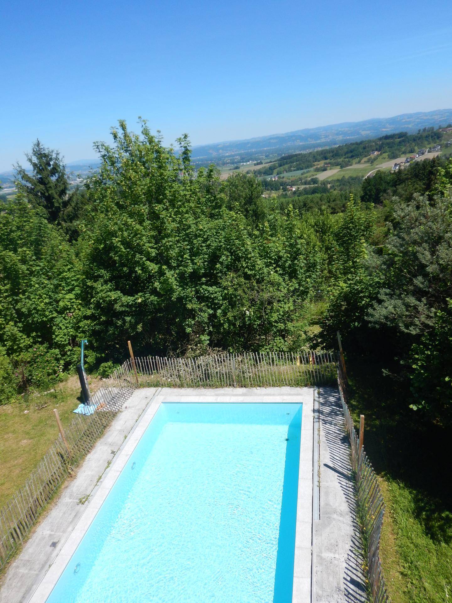 Blick von oben auf den Swimmingpool, umgeben von üppigem Grün und einer weiten Landschaft.