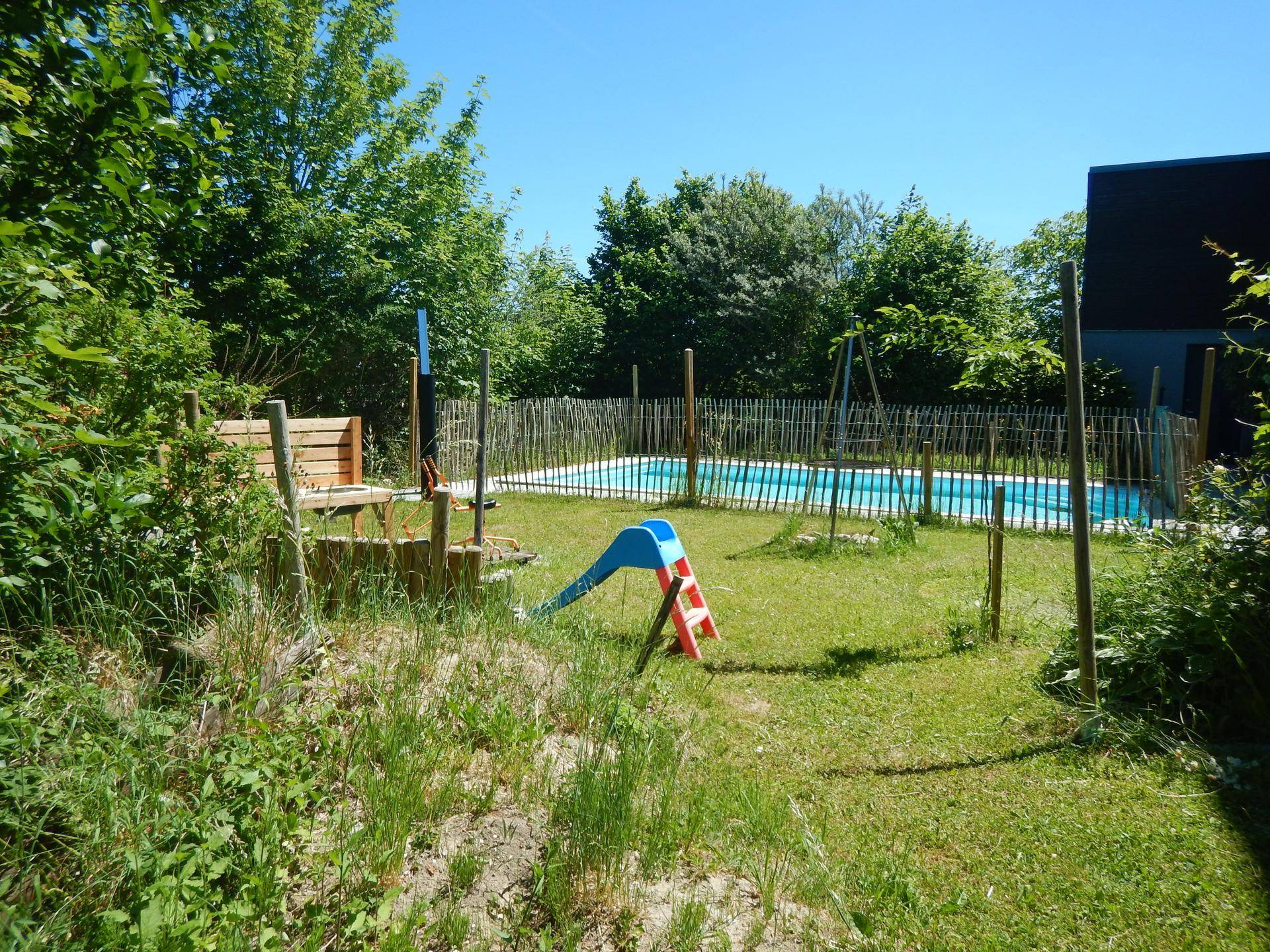 Gartenbereich mit Kinderrutsche, Sitzbank und Blick auf den Swimmingpool im Hintergrund.
