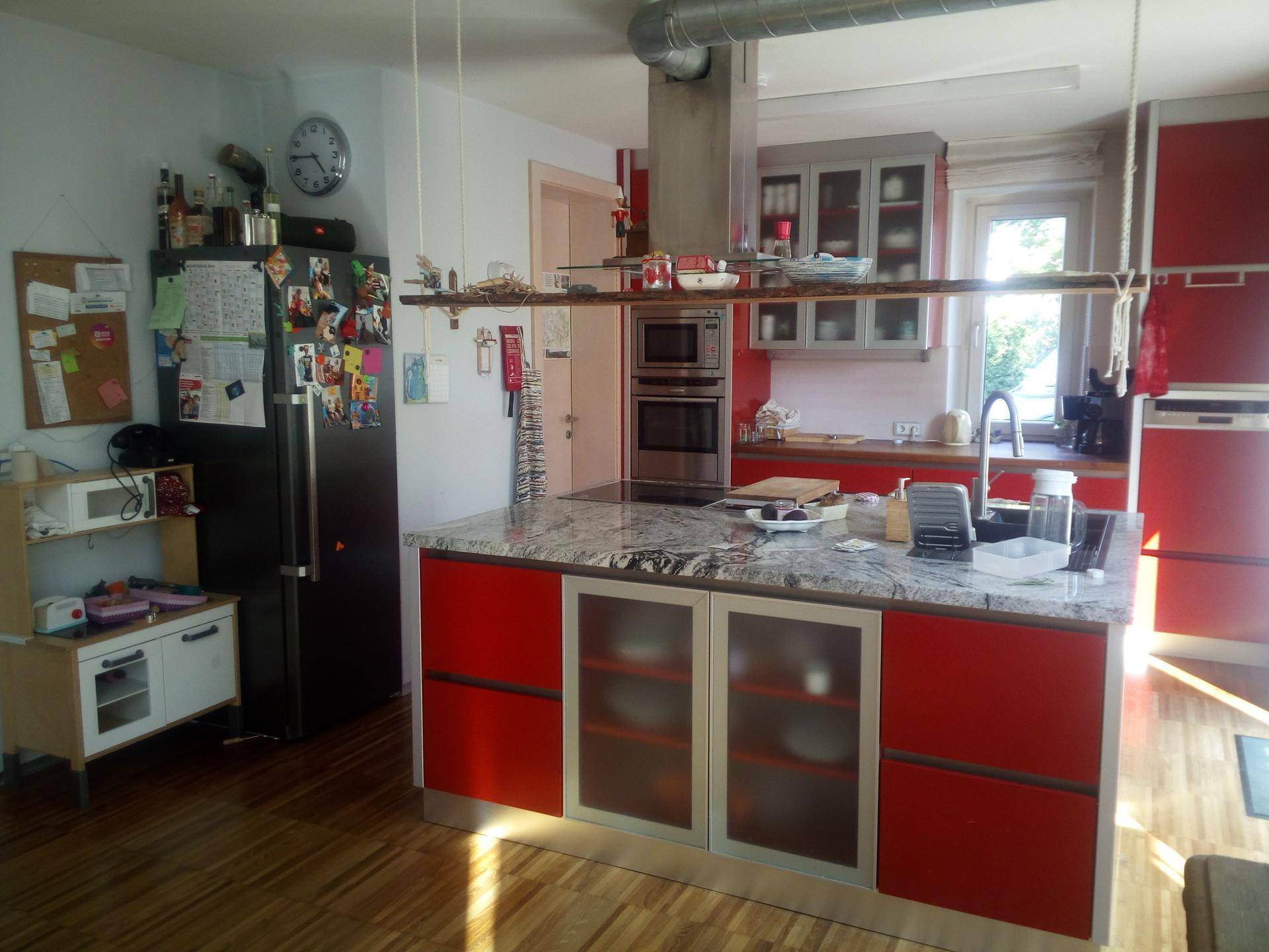 Moderne Küche mit roten Fronten, Kücheninsel mit Granitarbeitsplatte und integrierten Geräten.