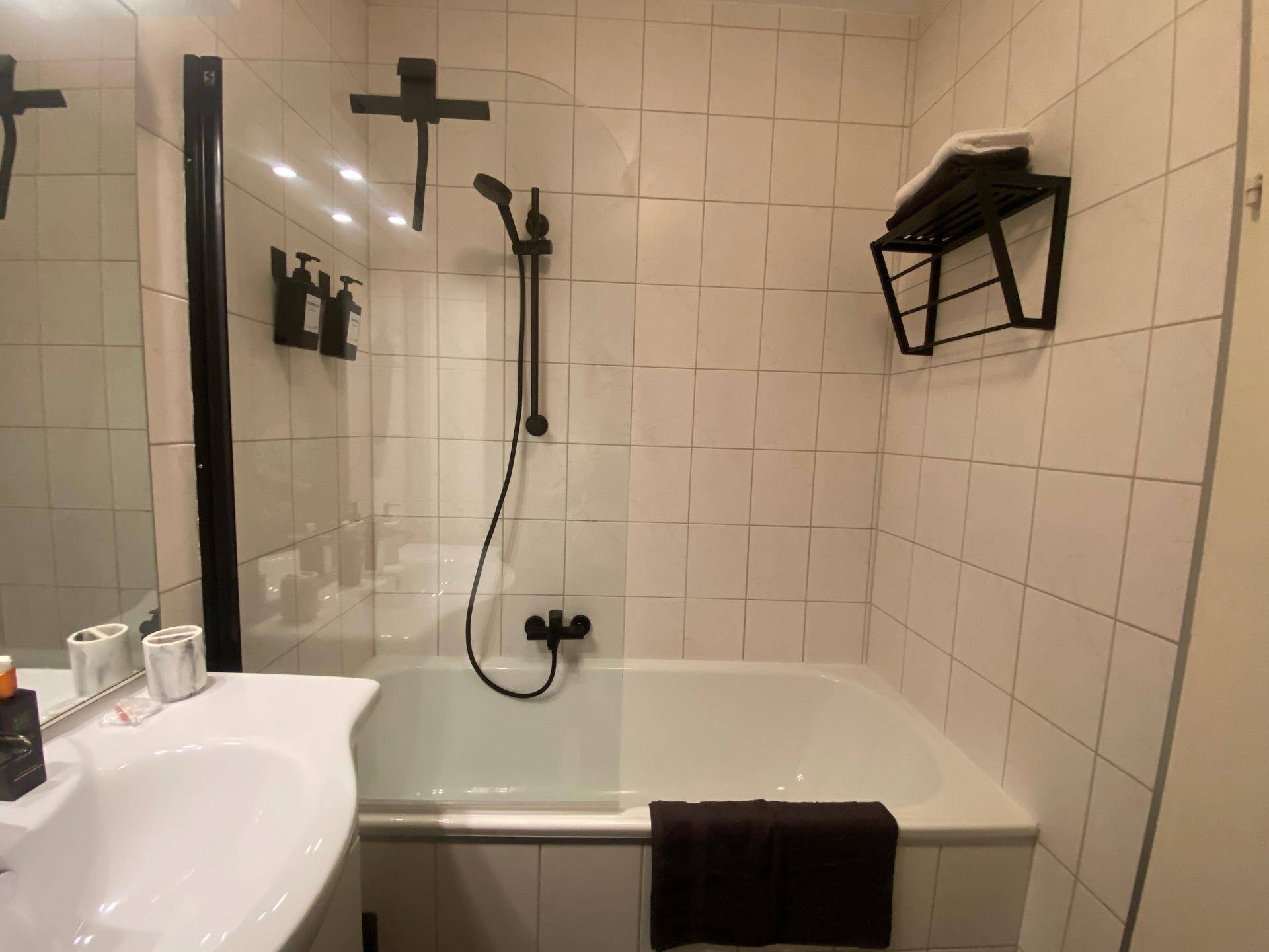 Badezimmer mit Badewanne, integrierter Dusche und weißen Wandfliesen.