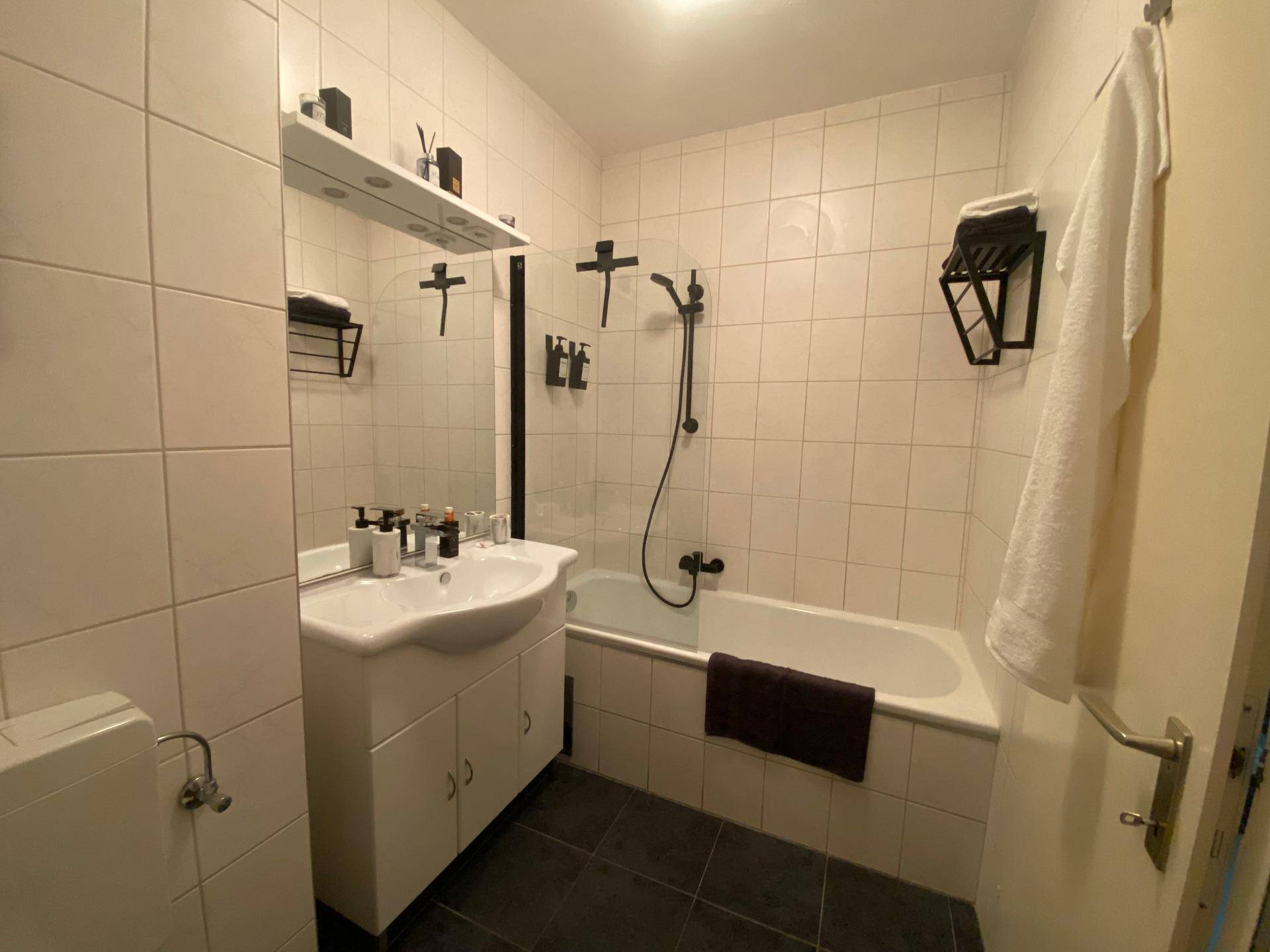 Funktionales Badezimmer mit Waschtisch, Spiegel und Badewanne mit Duschfunktion.