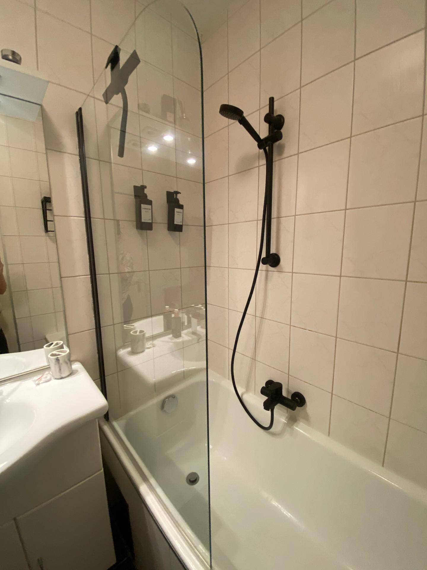 Badewanne mit Glasabtrennung und moderner Duscharmatur in Schwarz.