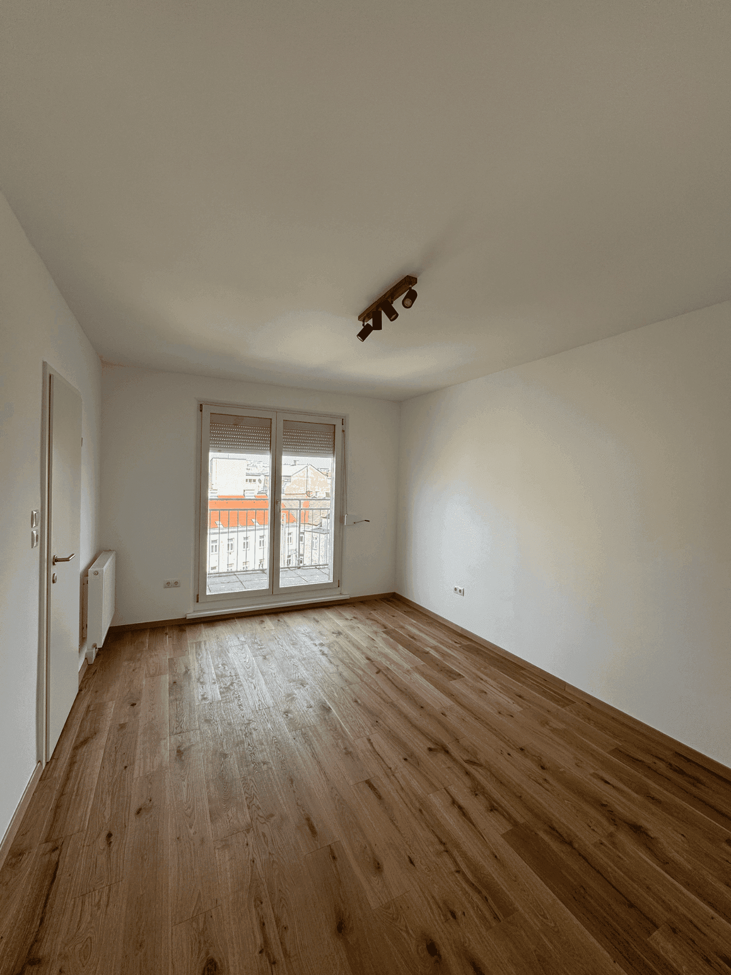 Helles Zimmer mit Holzboden und weiß gestrichenen Wänden, ausgestattet mit einem französischen Balkon.