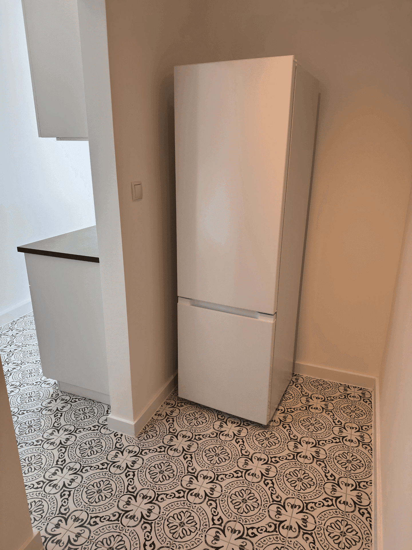 Weißer Kühlschrank in einer Küche mit auffälligen gemusterten Bodenfliesen und moderner Einrichtung.