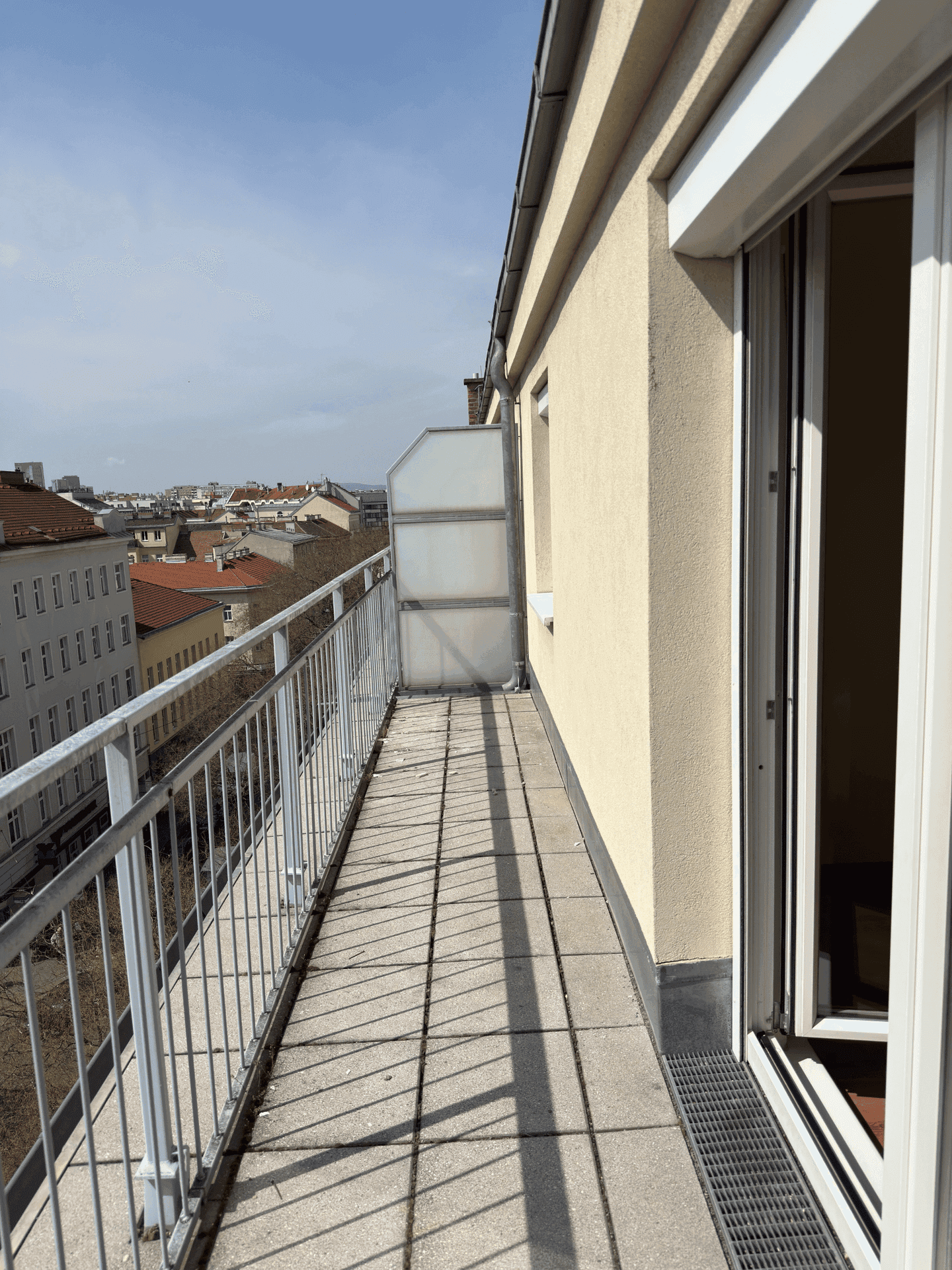 Langer, schmaler Balkon mit Fliesenboden und Metallgeländer, bietet einen Blick über die Dächer der Stadt.