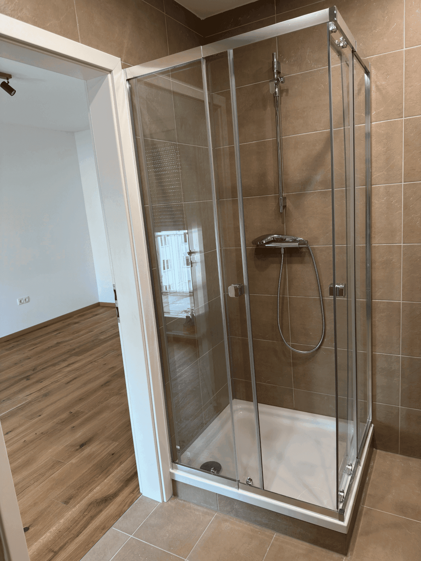 Badezimmer mit braunen Fliesen und einer modernen Duschkabine aus Glas, die zum Raum hin offen ist.