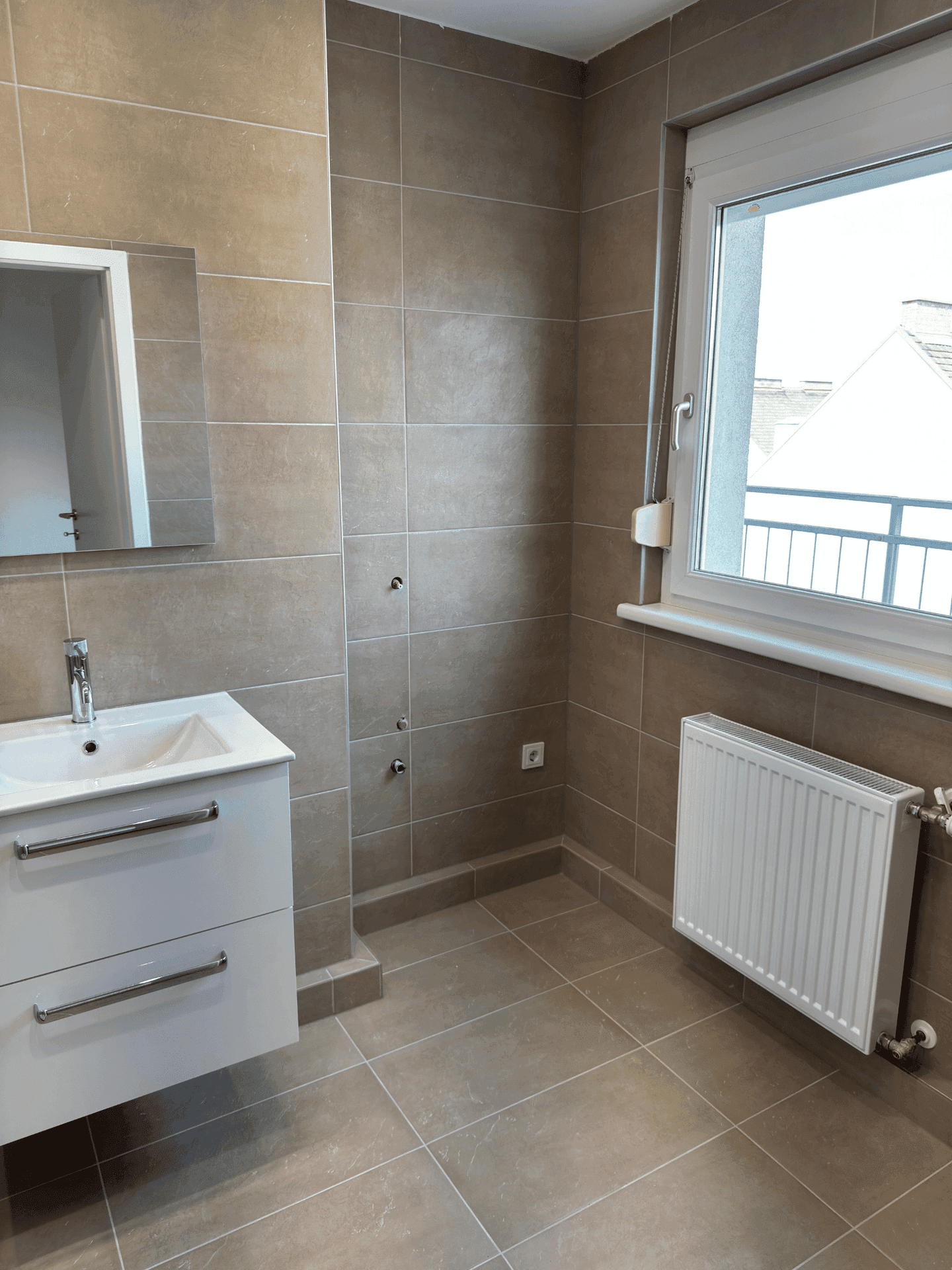 Modernes Badezimmer mit braunen Fliesen, Einzelwaschbecken, Spiegel und einem Fenster für Tageslicht.
