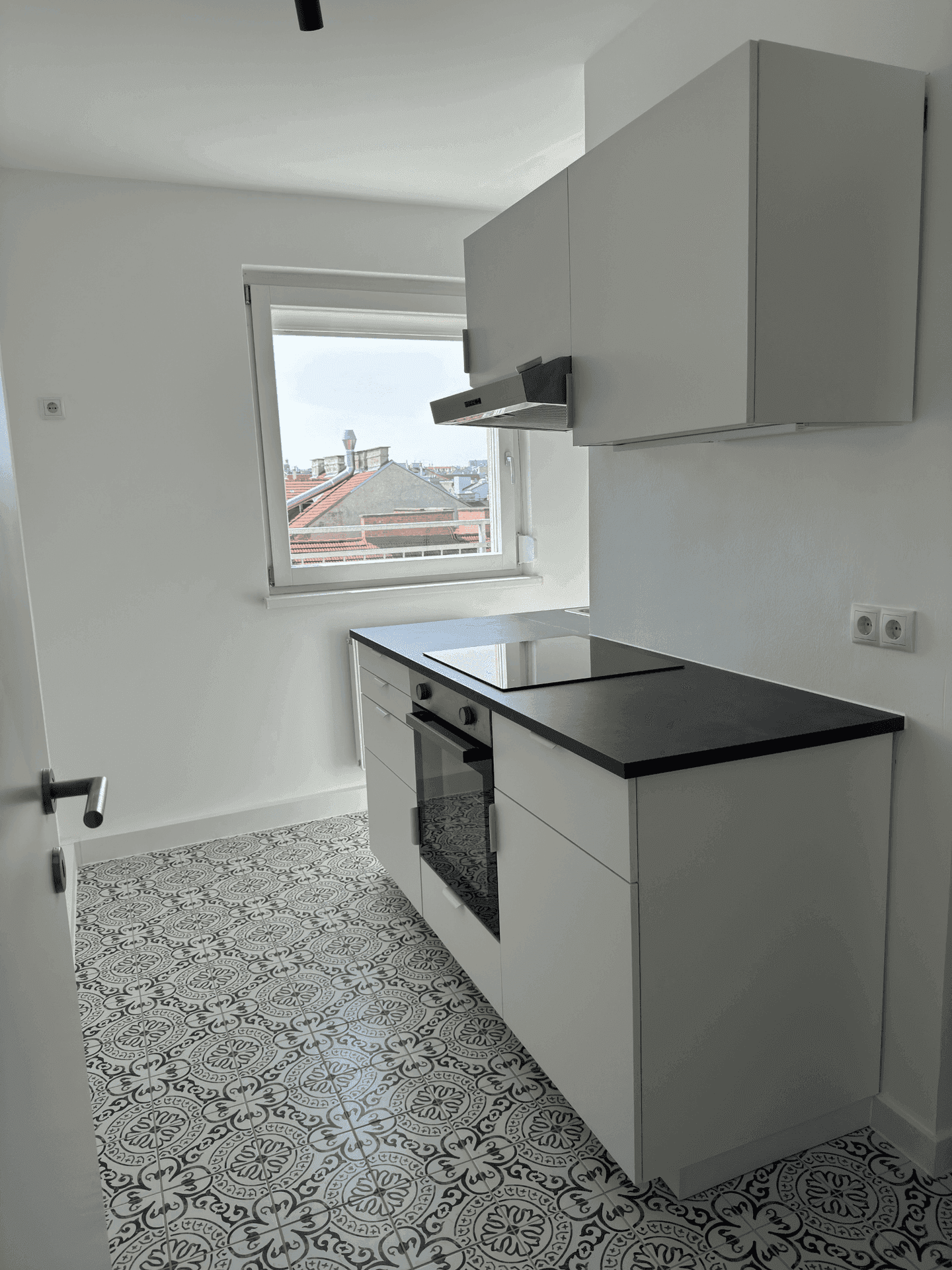 Moderne kleine Küche mit weißen Schränken, schwarzer Arbeitsplatte und Induktionskochfeld, mit Fenster.
