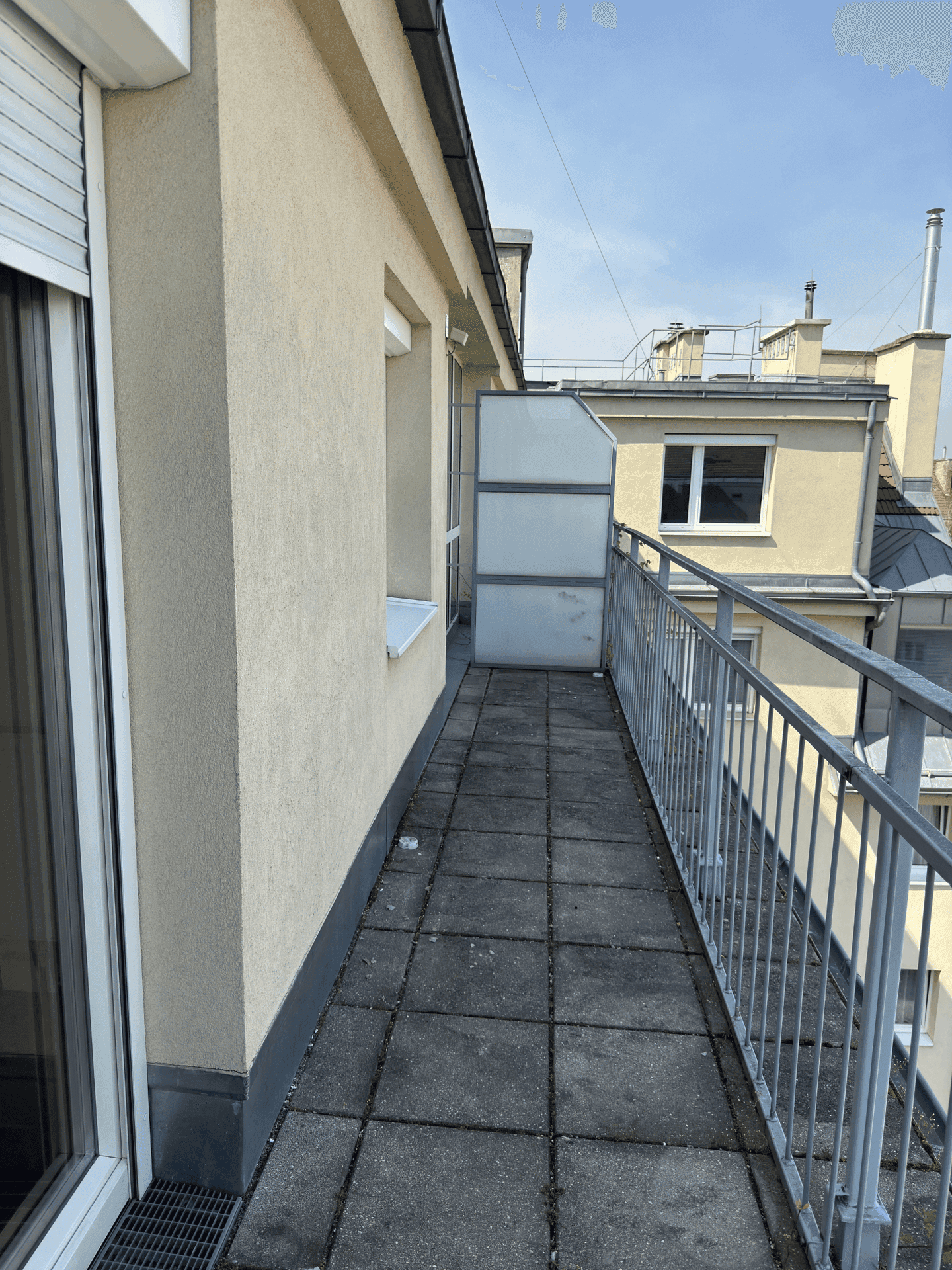 Schmaler Balkon mit Fliesenboden und Metallgeländer, bietet einen Ausblick auf die umliegenden Gebäude.