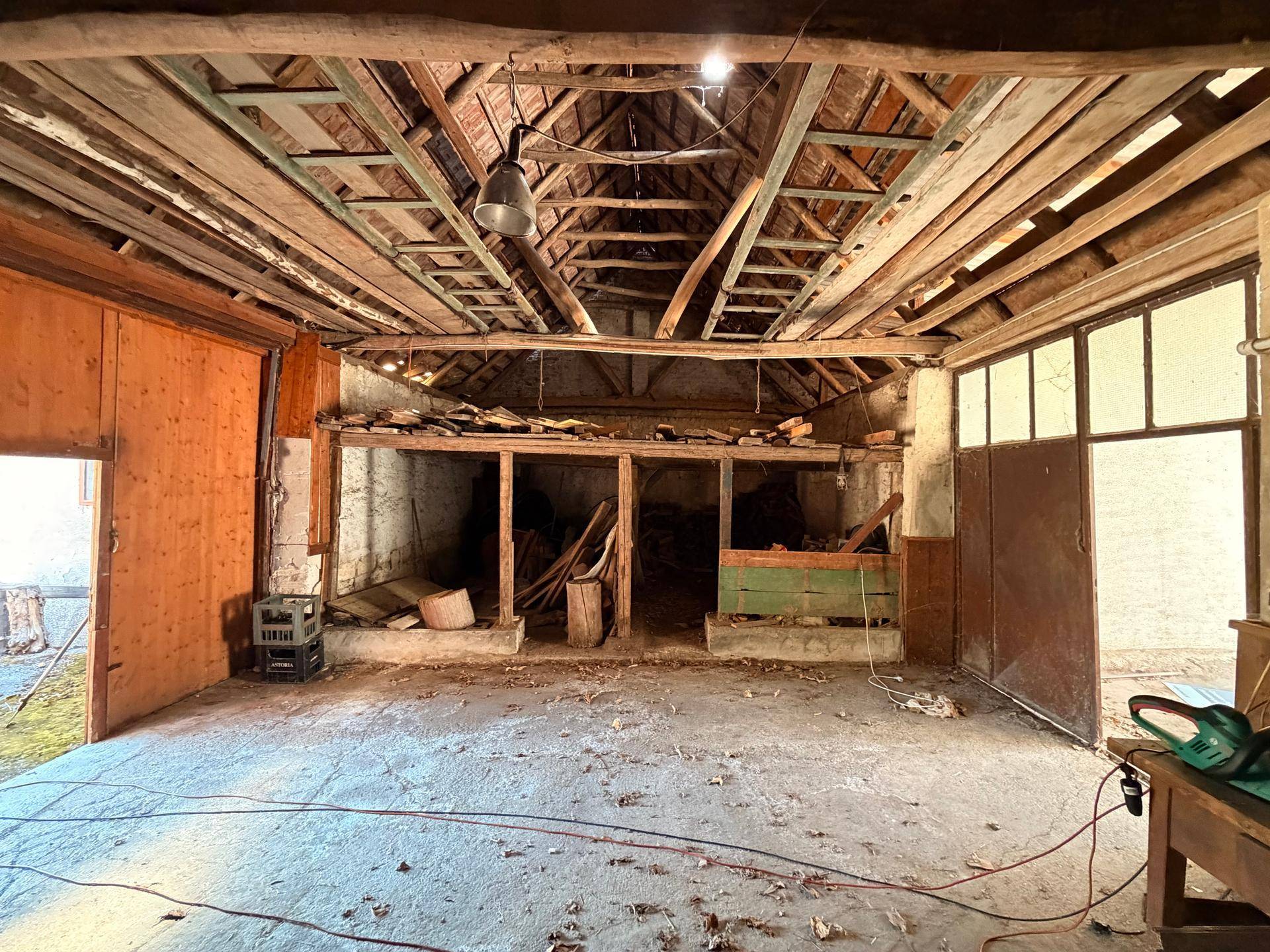 Geräumiger Werkstattbereich mit Holzbalken, Lagerregalen und großem Tor.