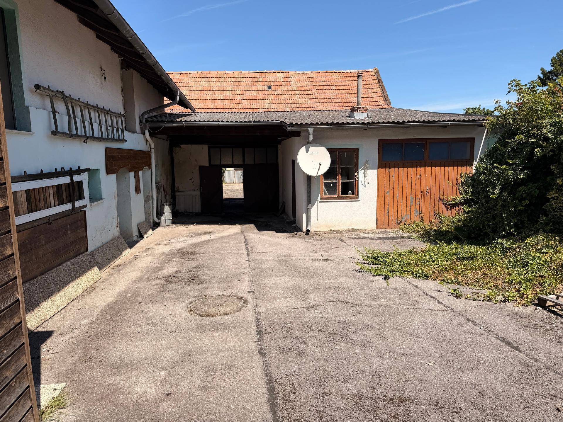 Seitenansicht eines Gebäudekomplexes mit offenem Unterstand und Zufahrt.