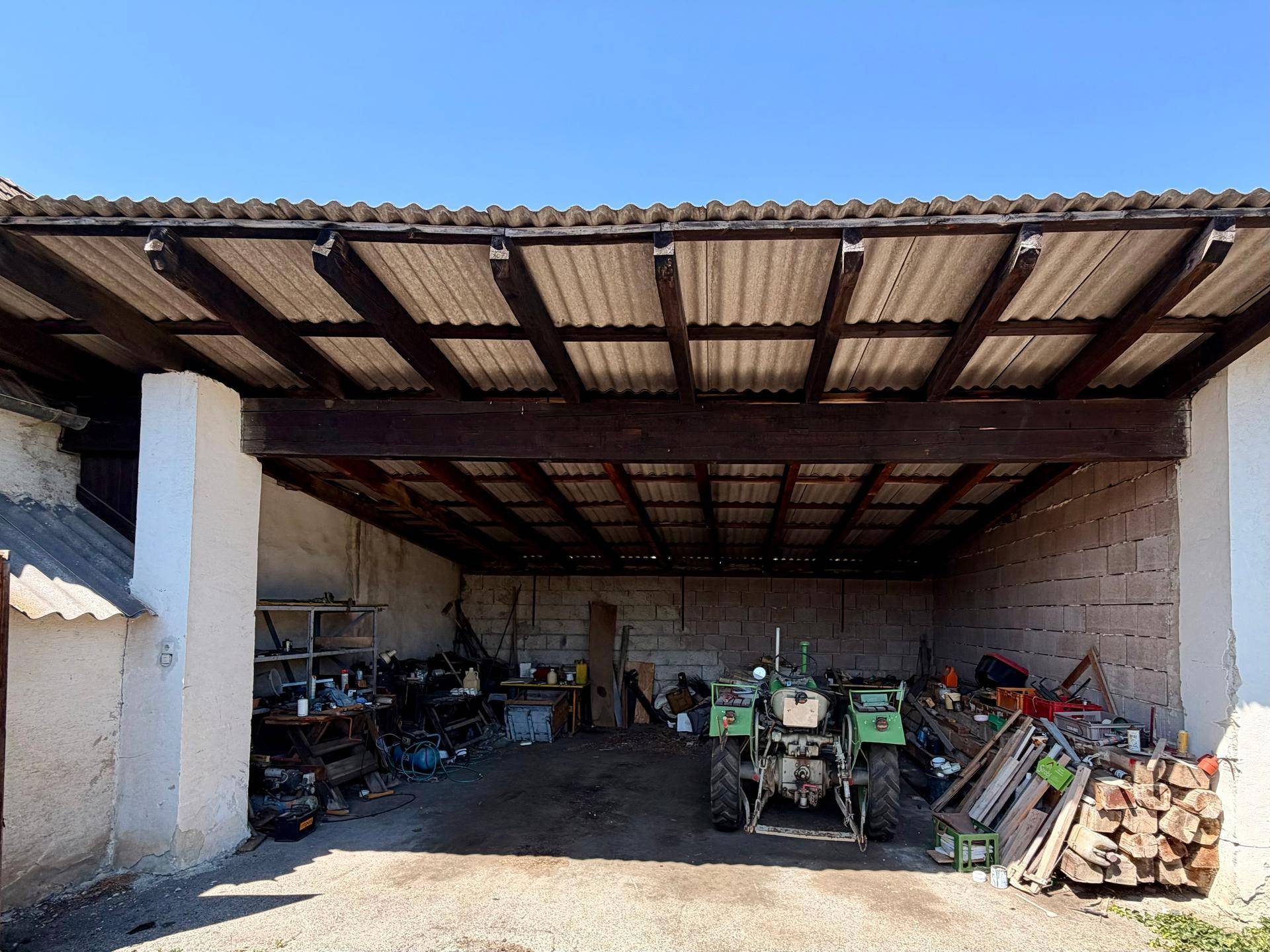 Großer überdachter Bereich, genutzt als Garage oder Lagerfläche, mit Traktor.