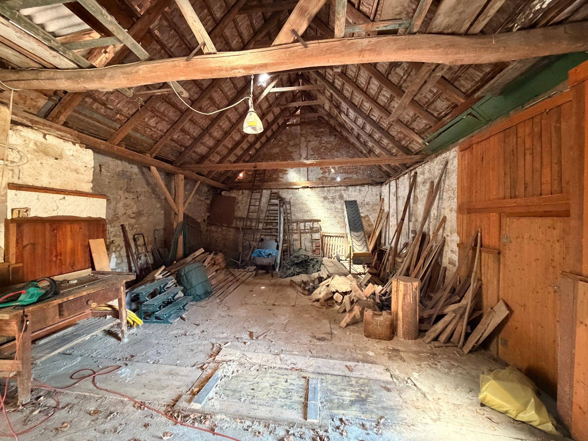 Rustikaler Innenraum einer Scheune mit Holzbalken, Lagerflächen und Werkzeugen.