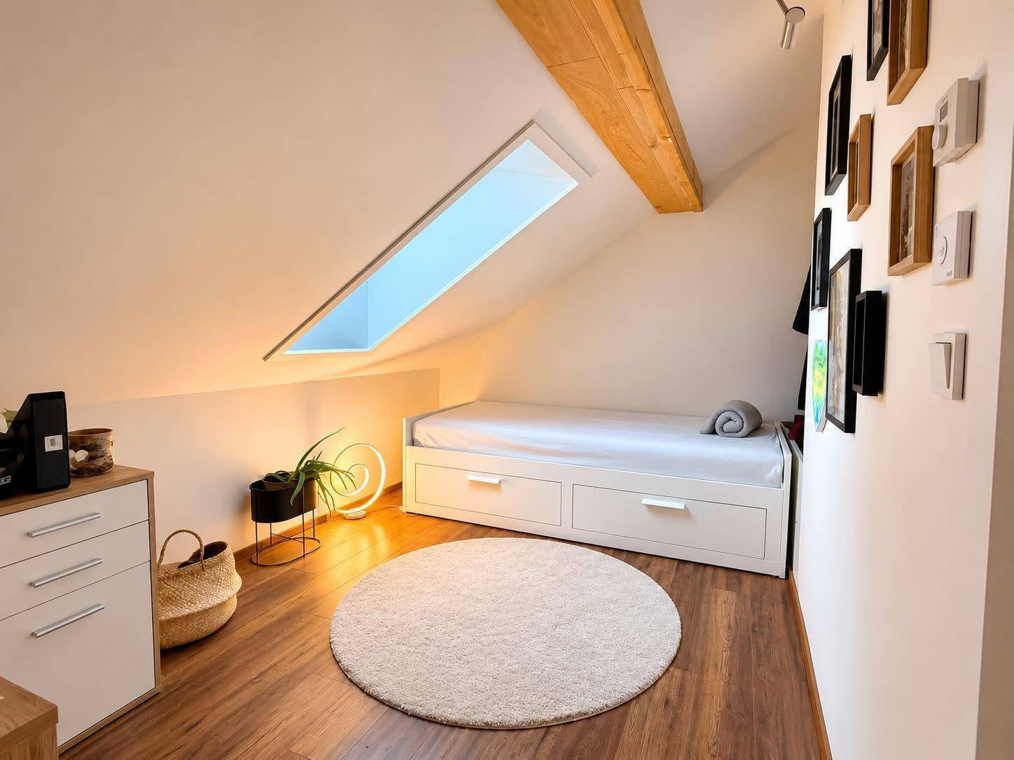 Helles Schlafzimmer im Dachgeschoss mit Einzelbett, Holzbalken und Dachfenster.