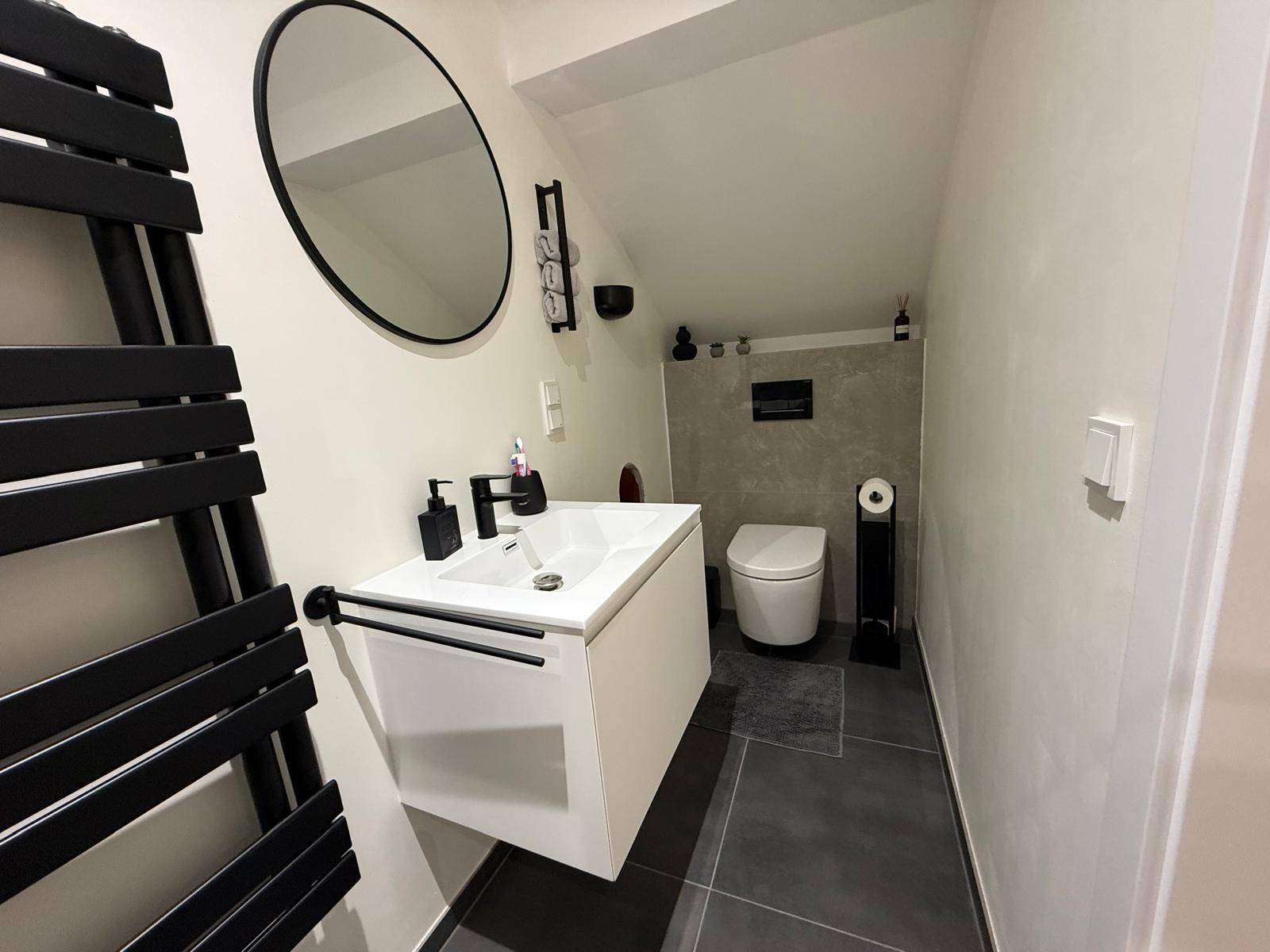 Modernes Gäste-WC im Dachgeschoss mit Schräge, Heizkörper und rundem Spiegel.